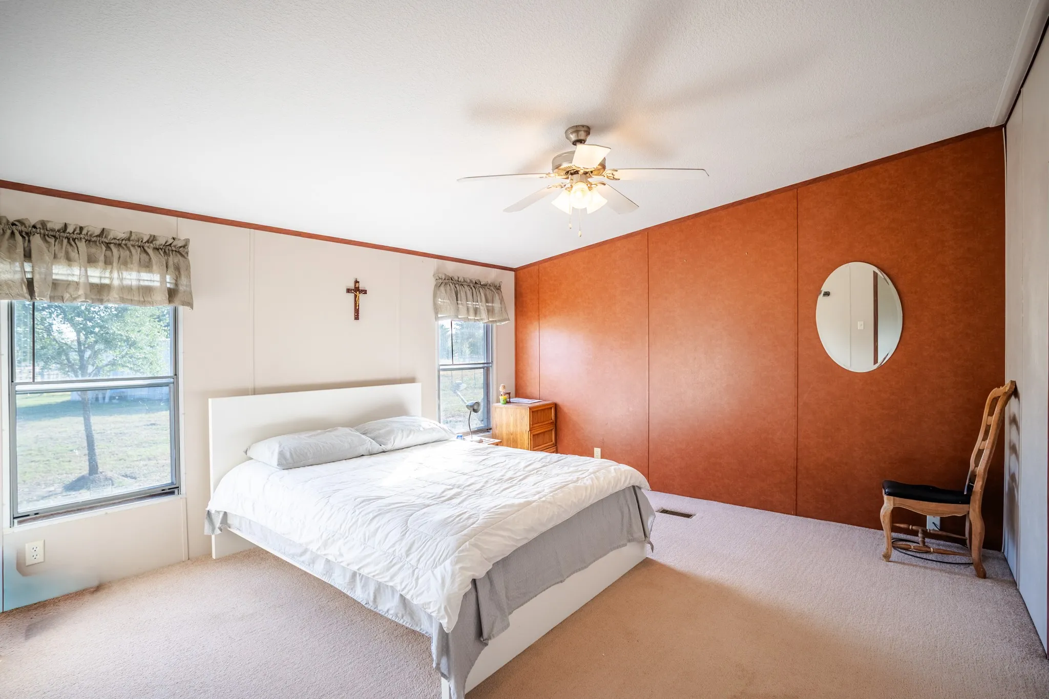 Carpeted flooring throughout, warm-toned accent wall, multiple windows, and a ceiling fan with integrated lighting