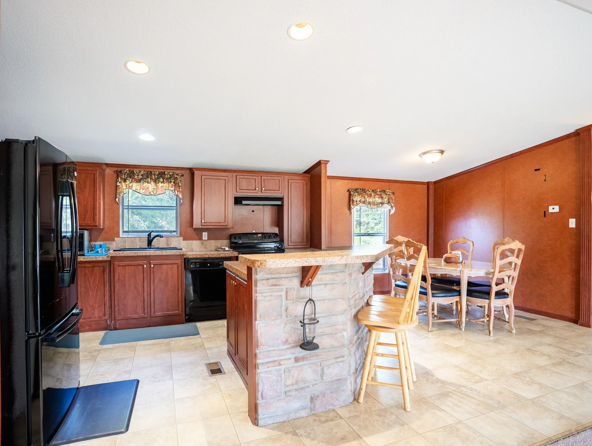 Kitchen featuring wood cabinetry, black appliances, tile flooring, stone-clad breakfast bar, and recessed lighting