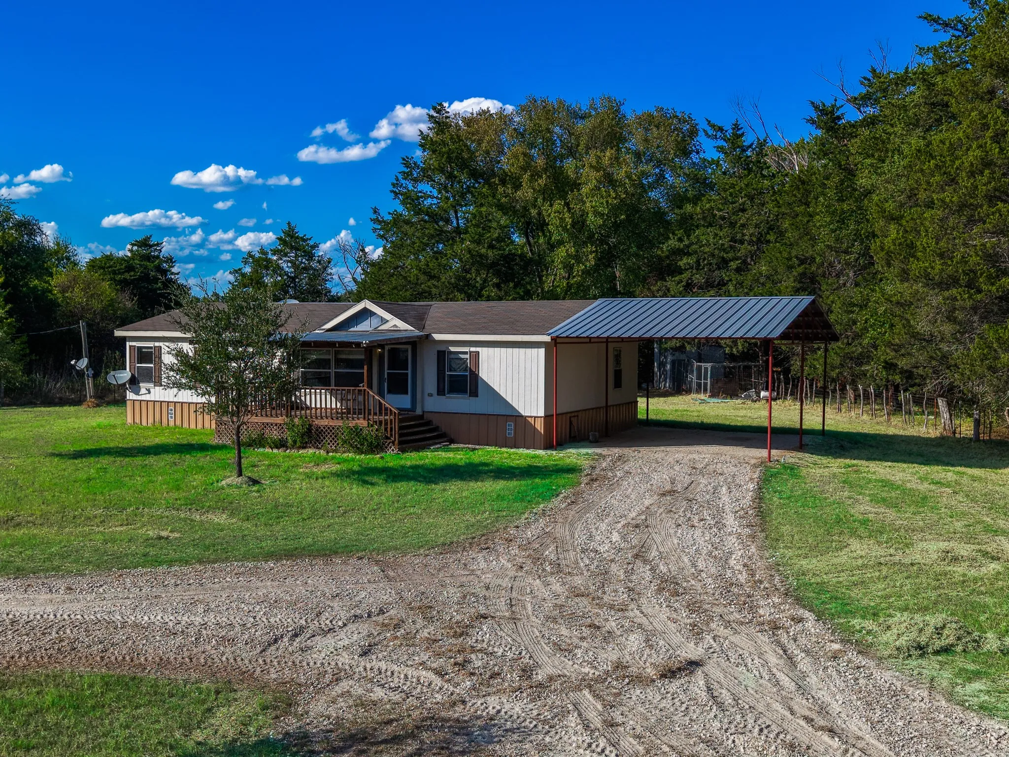 Single-story home featuring a covered front porch with wood railings and steps, a gravel driveway, and a detached metal carport