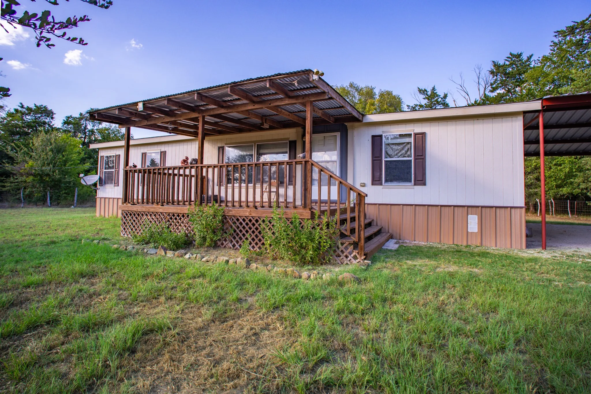 Outdoor wood deck, covered porch with corrugated roof, wood privacy railing, wood lattice skirting, and attached carport