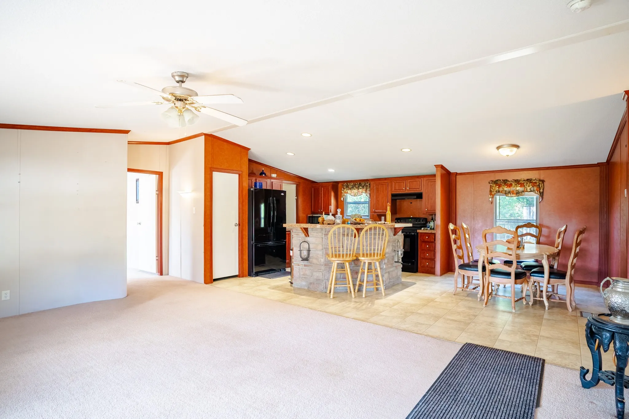 Expansive open-concept living area featuring a ceiling fan, kitchen with wood-finish cabinetry, and a stone-clad kitchen island
