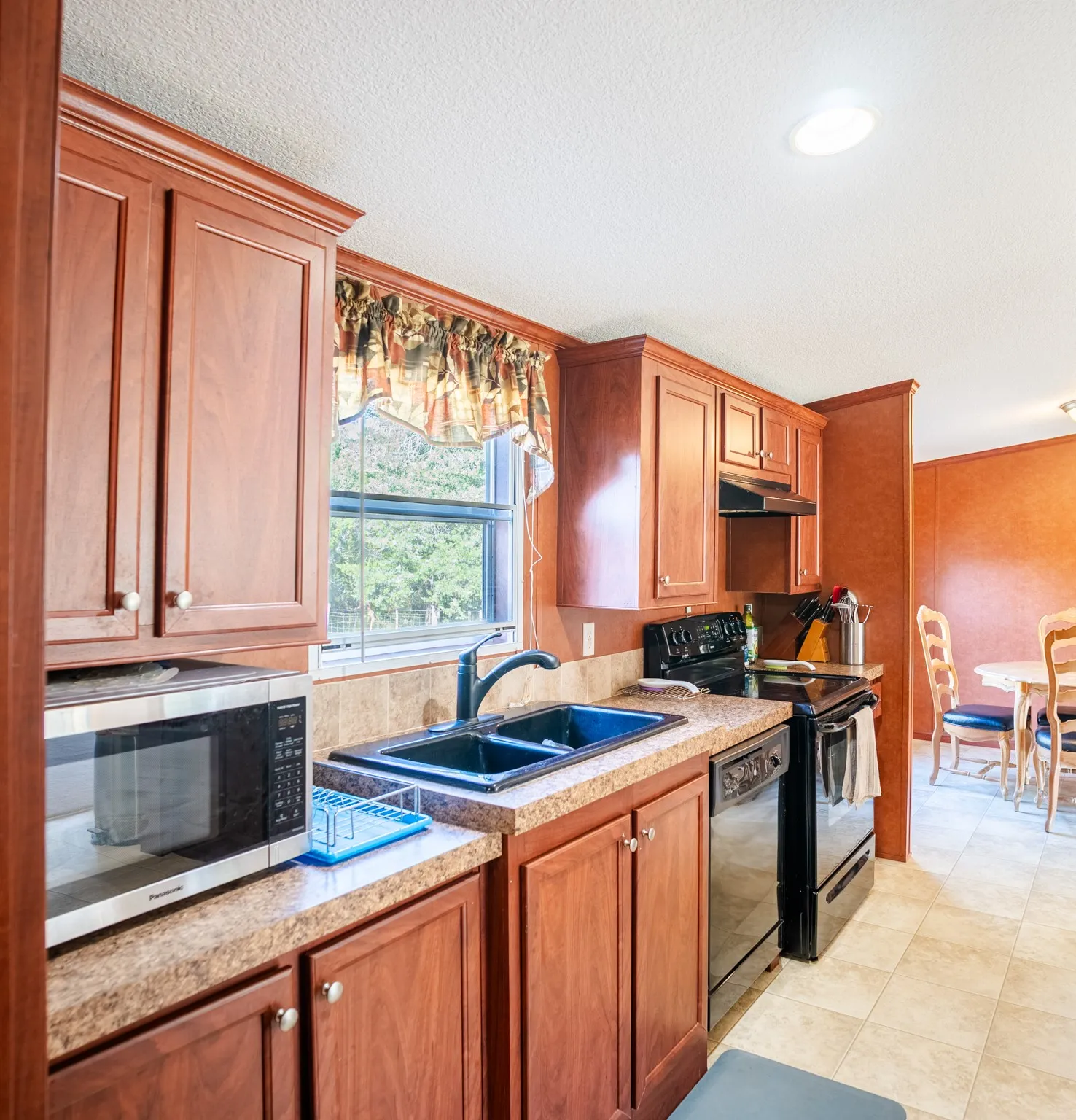 Kitchen featuring wood-finish cabinetry, a double basin sink with a black faucet, black appliances, and neutral-toned countertops