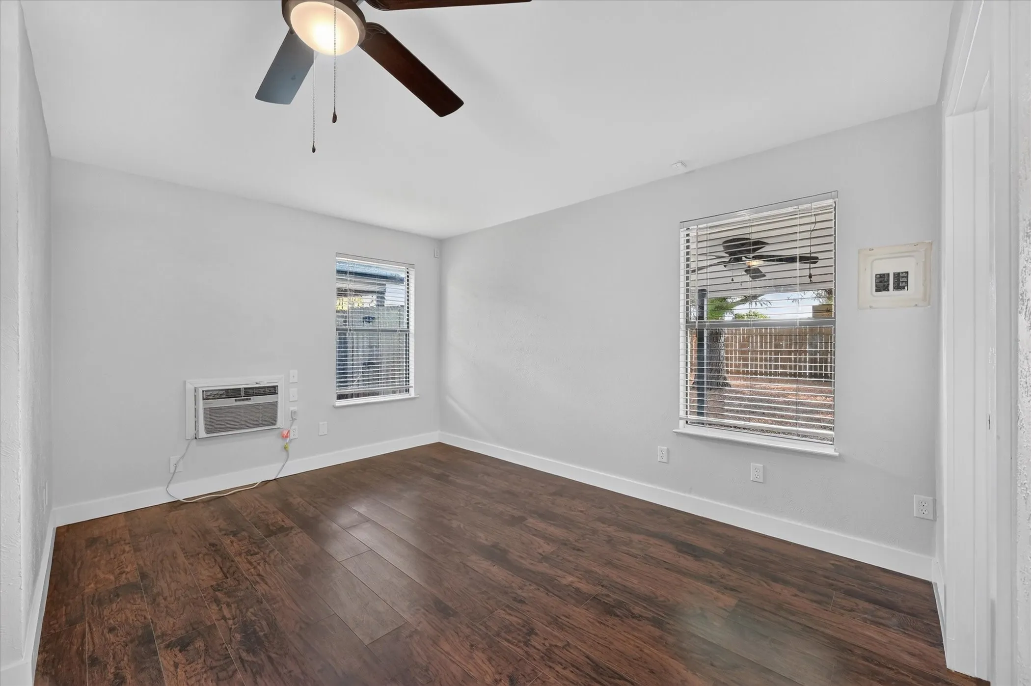 Wood-finish flooring, two windows with blinds, and a ceiling fan with integrated lighting