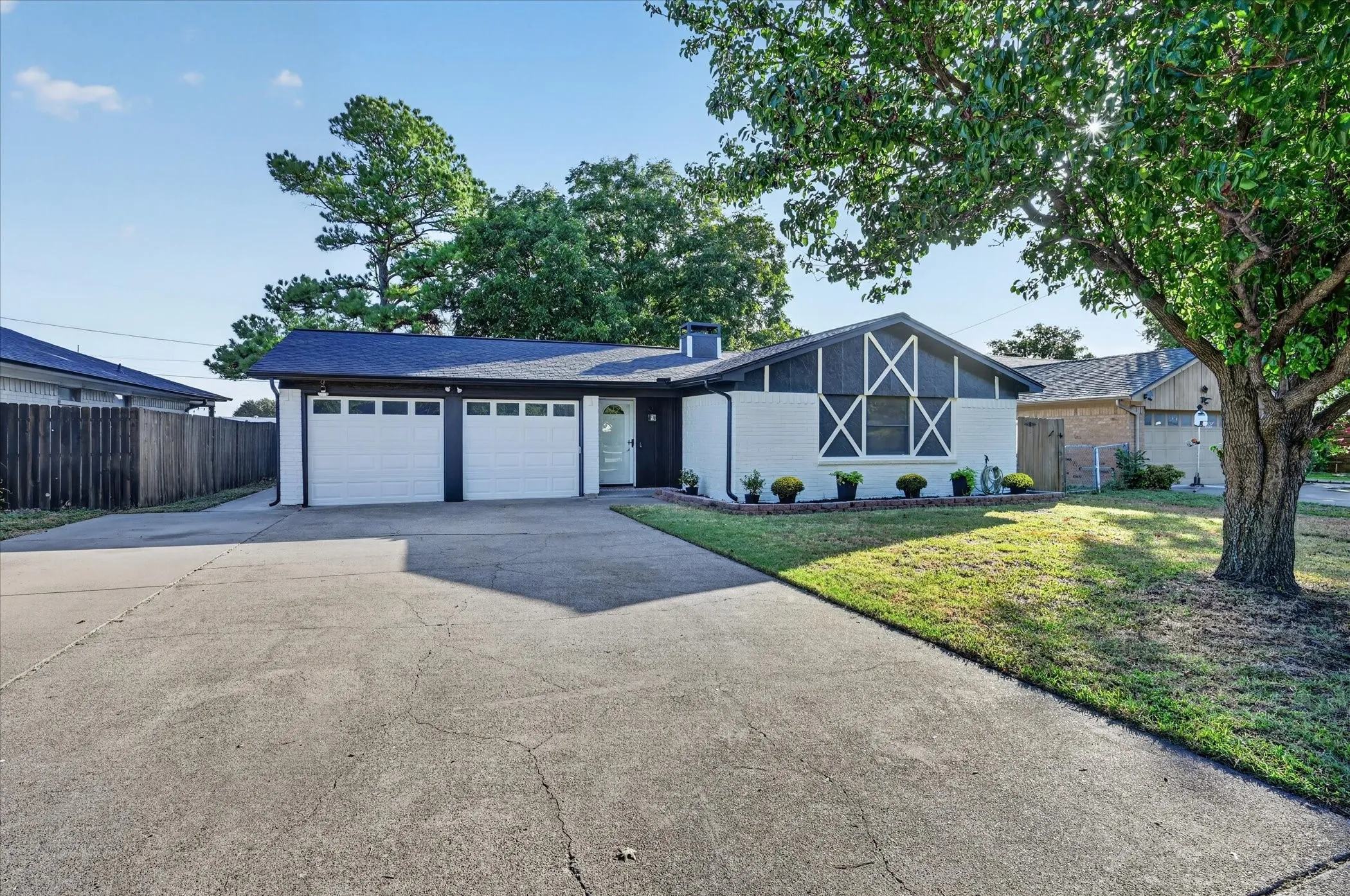 White brick facade with dark trim, two-car garage, concrete driveway, and mature trees