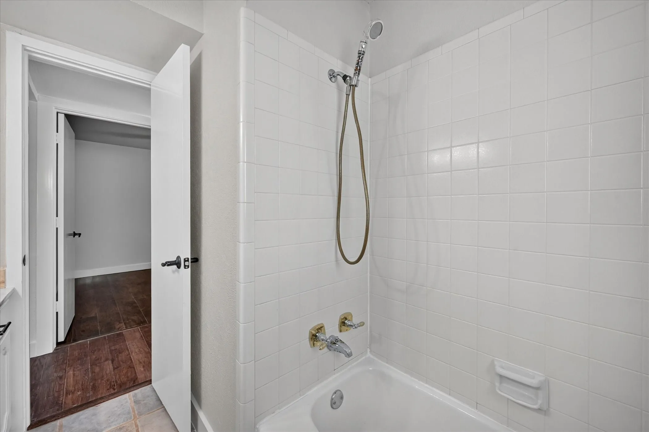 Bathtub with white tile surround and a handheld shower head