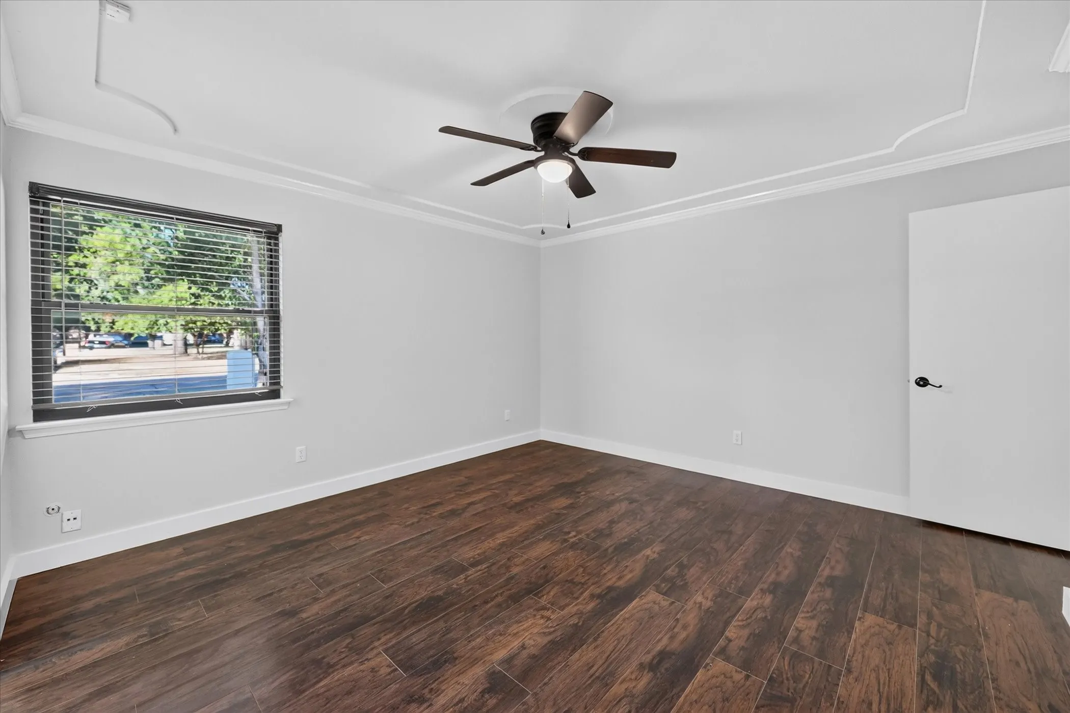 Wood-finish flooring, ceiling fan, window with blinds, crown molding, white baseboards