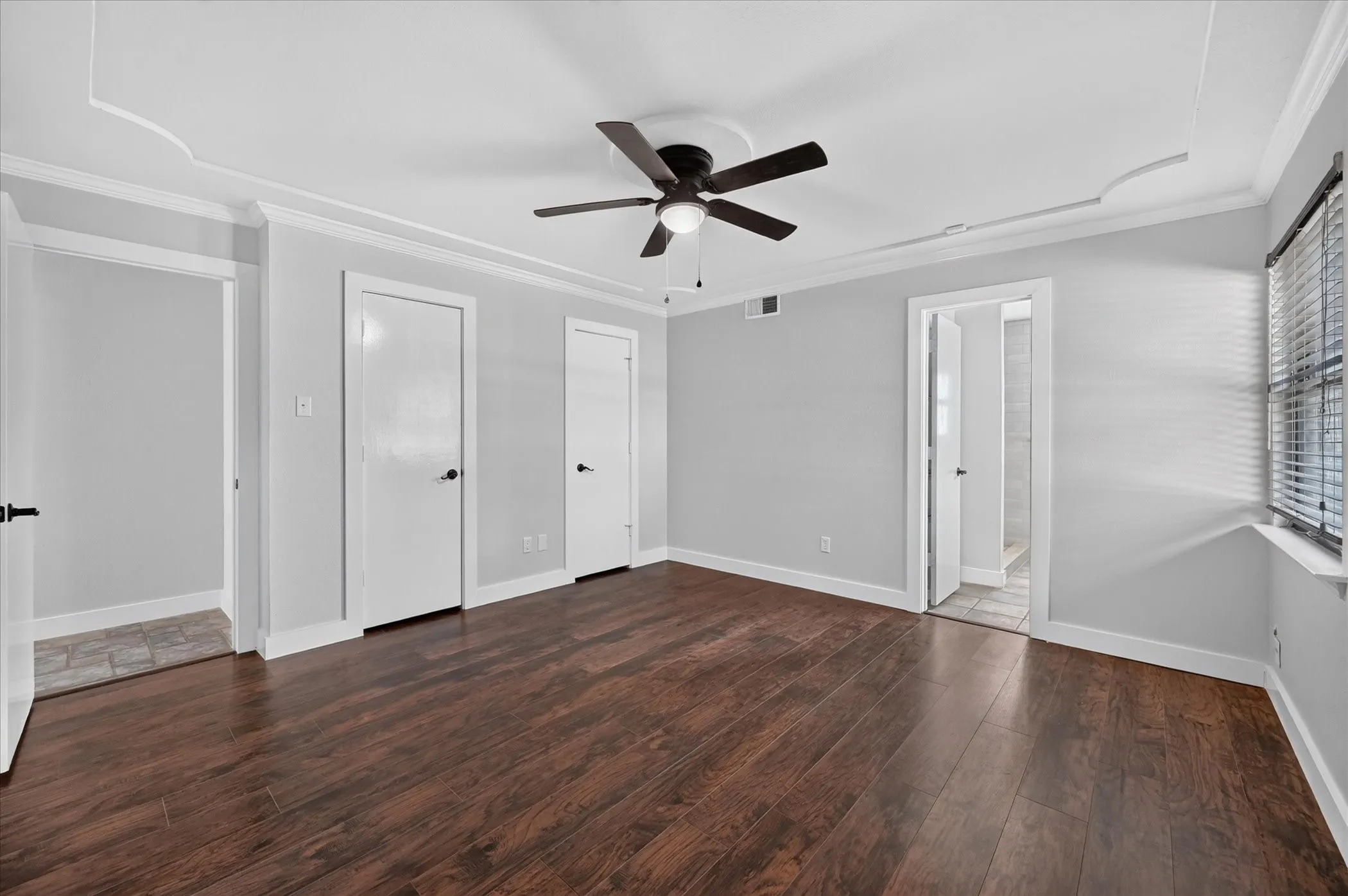 Wood-finish flooring, ceiling fan, crown molding, white trim, and window blinds