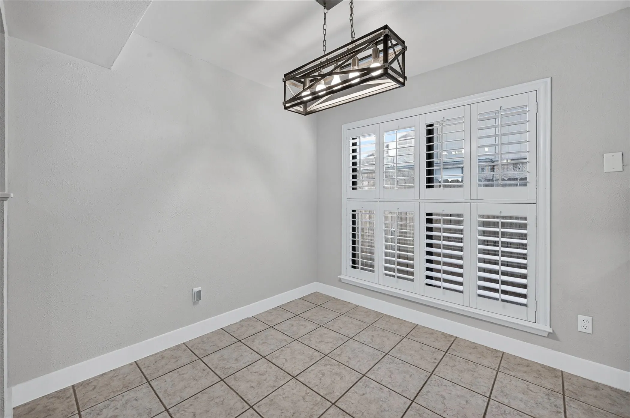 Large window featuring plantation shutters, overhead linear chandelier with metal framing, and tile flooring