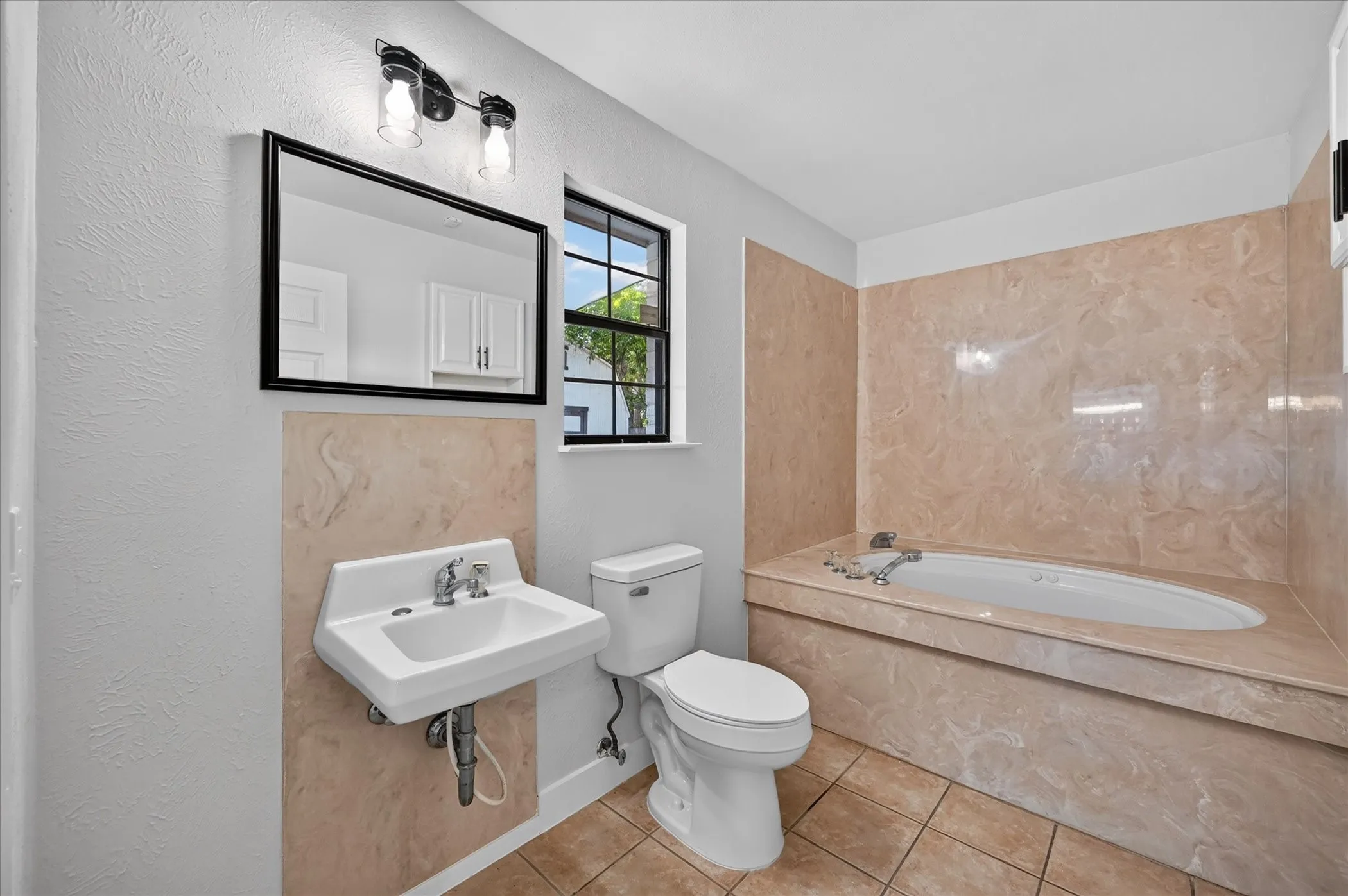 Built-in soaking tub with a tiled surround, wall-mounted vanity mirror, and a wall-mounted sink