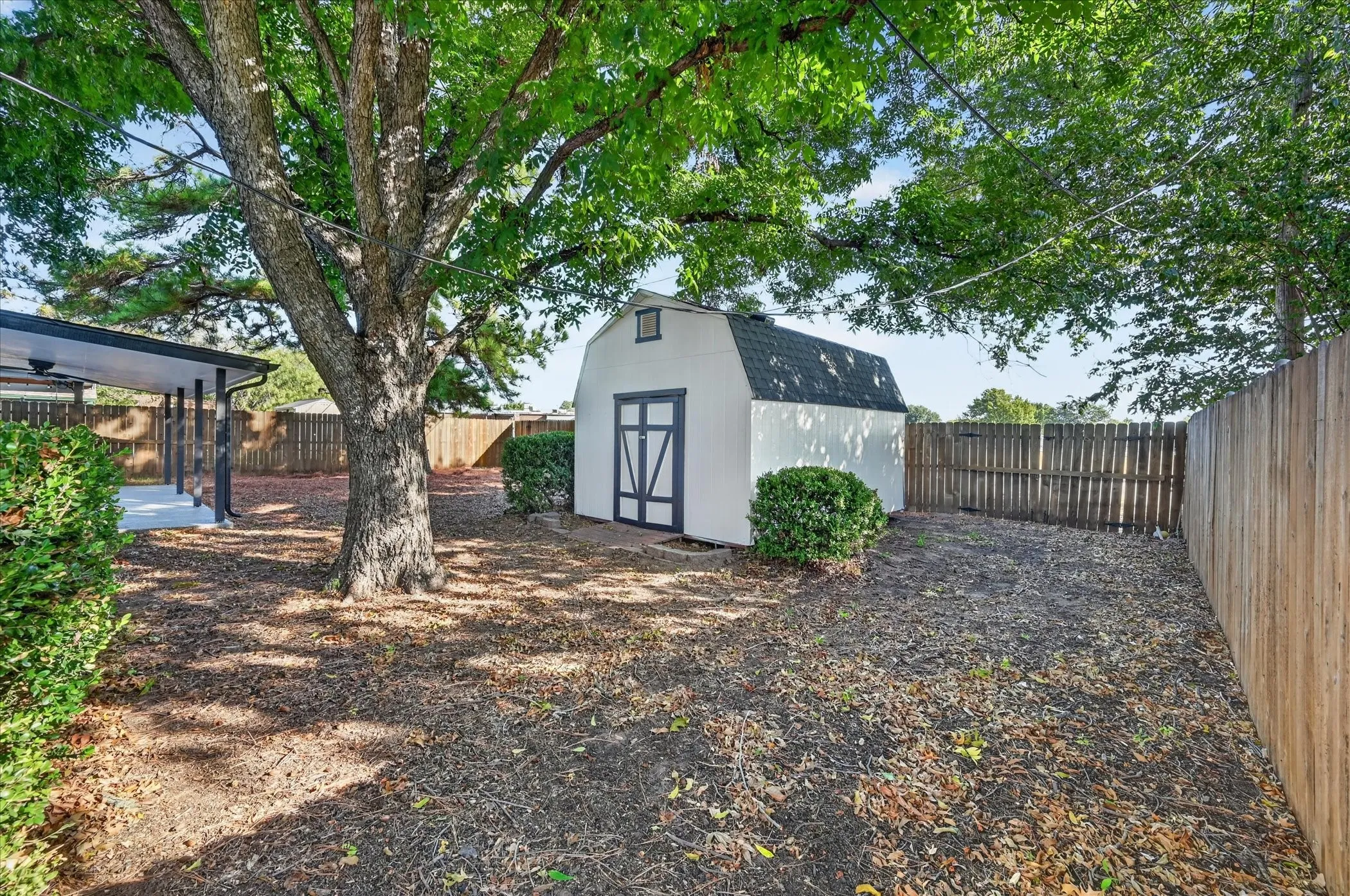 Spacious backyard with mature trees, a white barn-style storage shed, and wooden privacy fencing