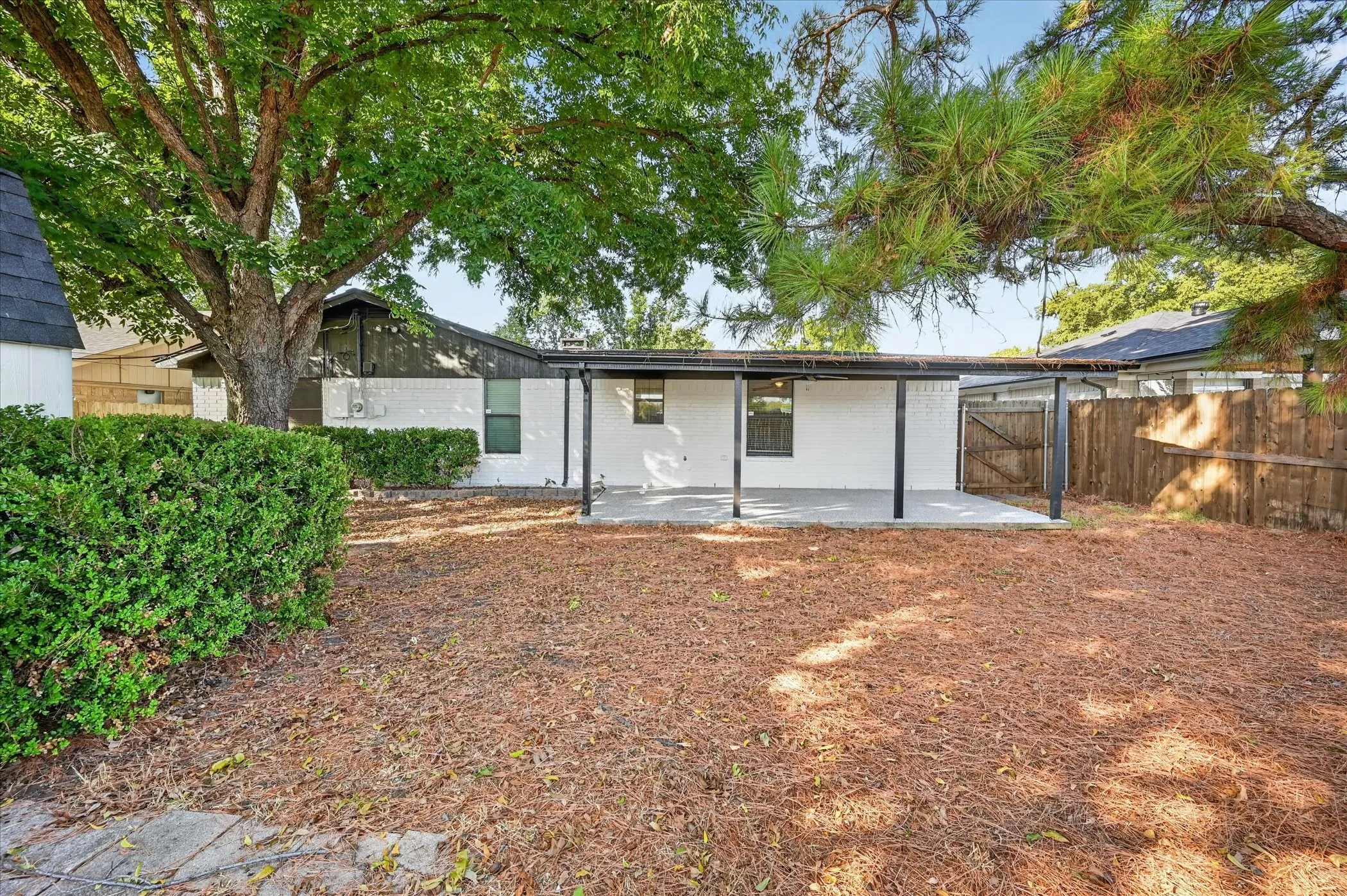 Covered patio with concrete flooring, mature perimeter landscaping, and wood fencing