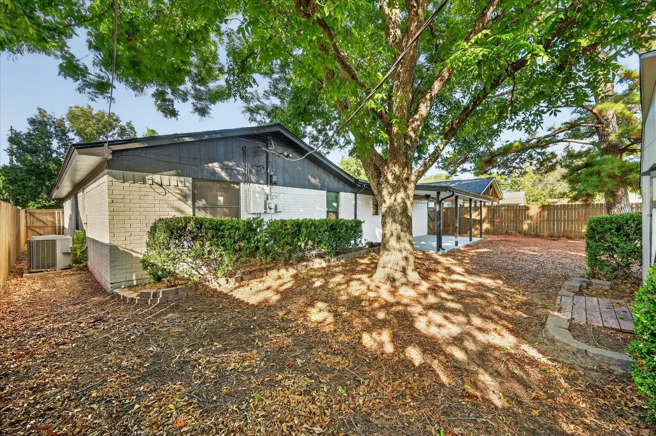 Expansive backyard featuring mature trees, wood fencing, and a covered patio area