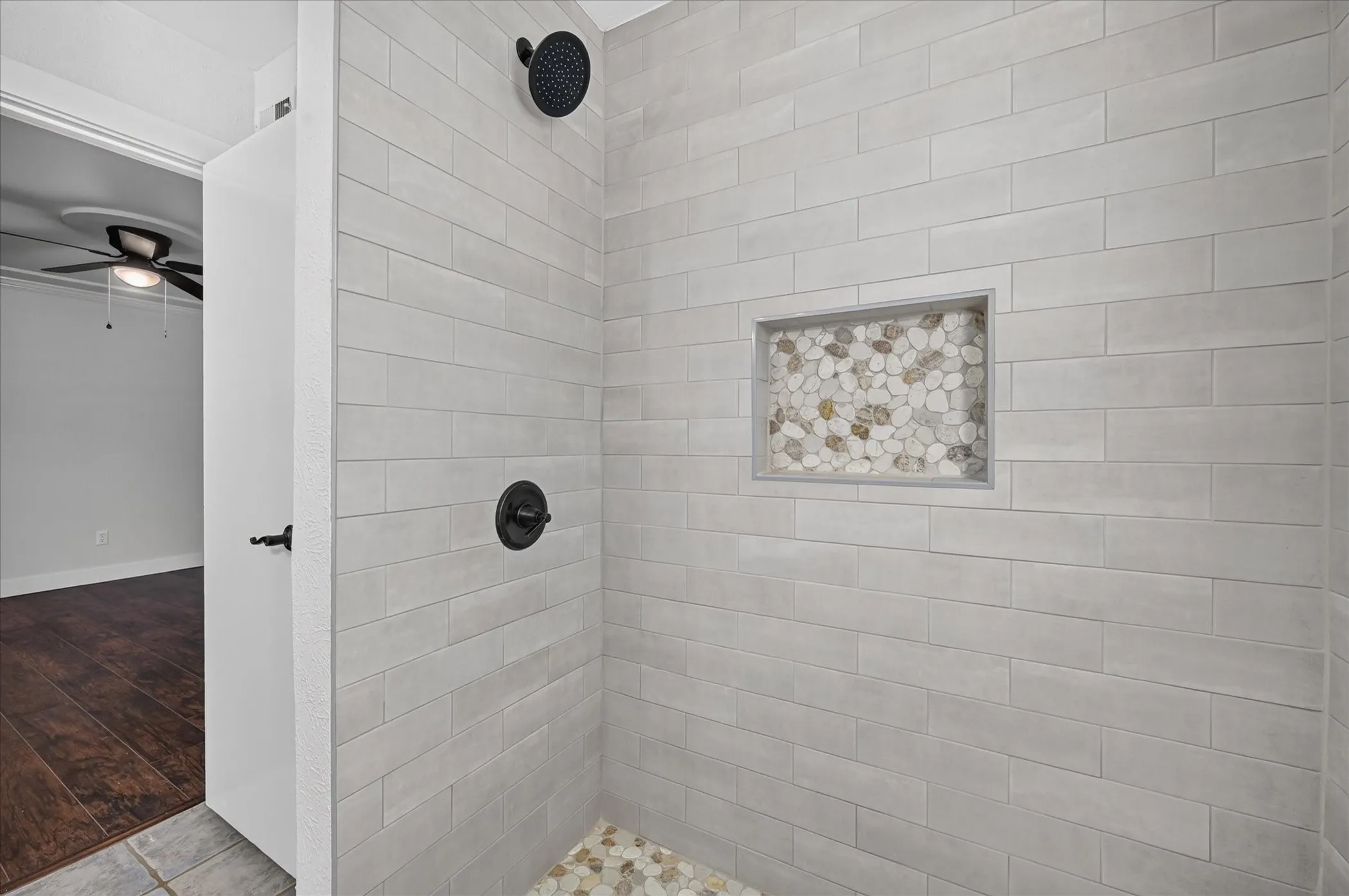 Shower featuring subway tile walls, a built-in niche with pebble tile, a dark-finish shower head, and coordinating dark-finish controls