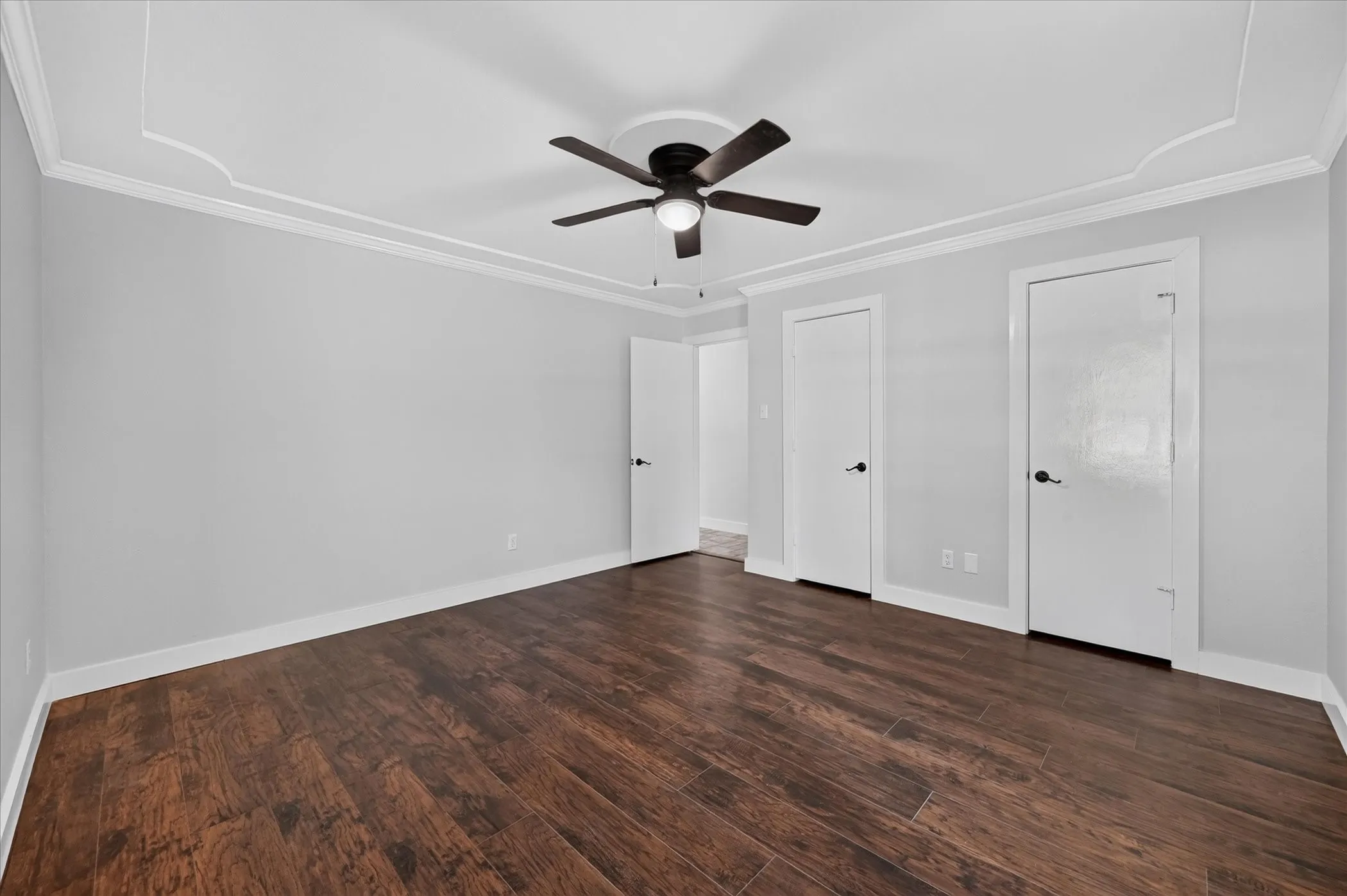 Wood-finish flooring, crown molding, tray ceiling, and a ceiling fan