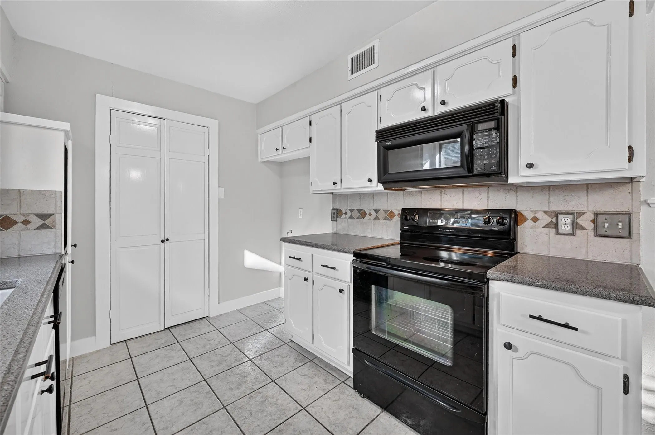 White cabinetry with dark hardware, black appliances, tile flooring, and patterned tile backsplash