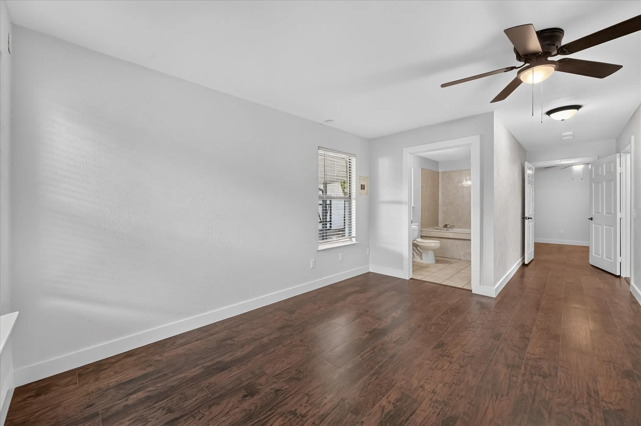 Expansive room featuring wood-finish flooring, a ceiling fan, and a window with blinds