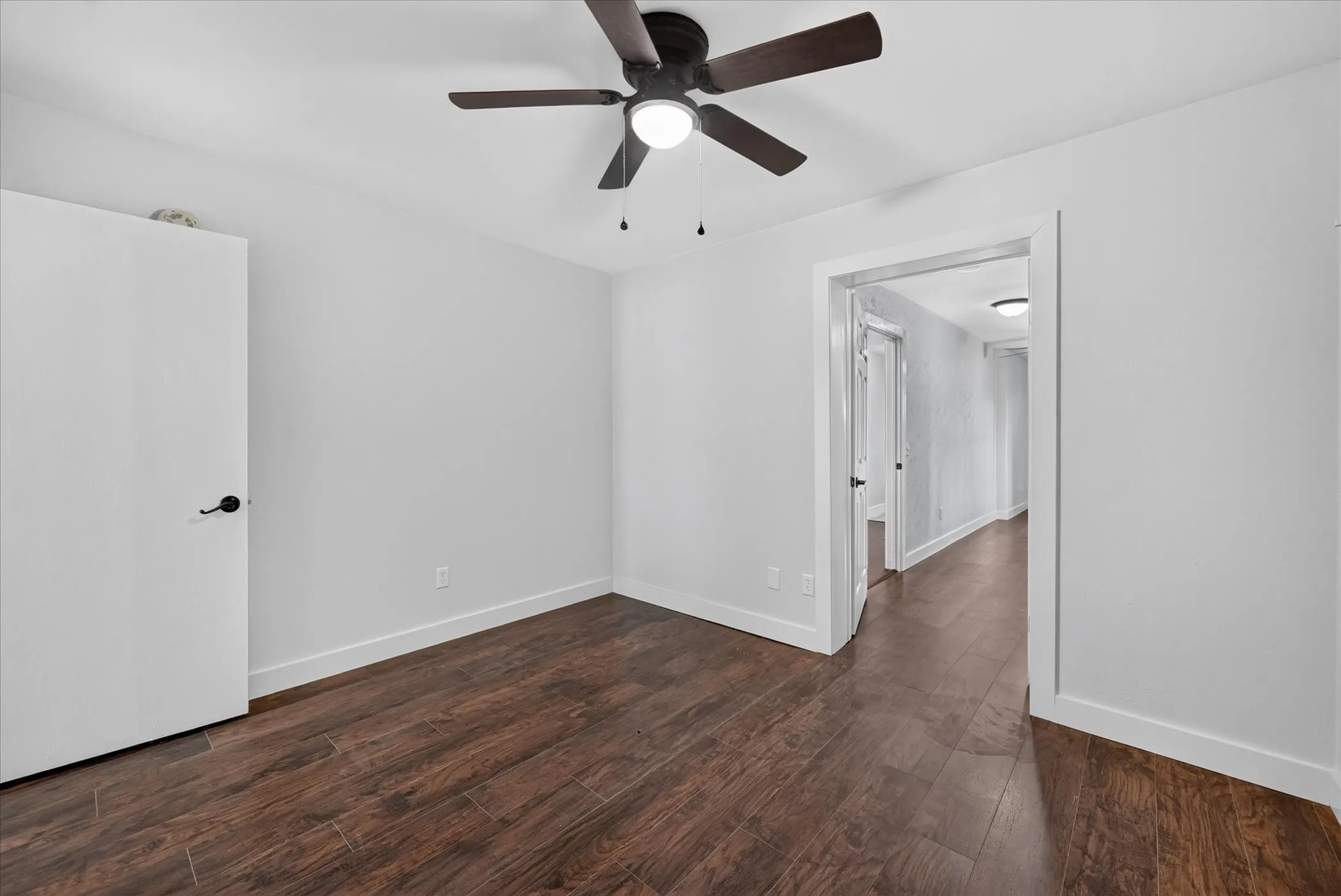 Wood-finish flooring, white walls, and a ceiling fan with integrated lighting
