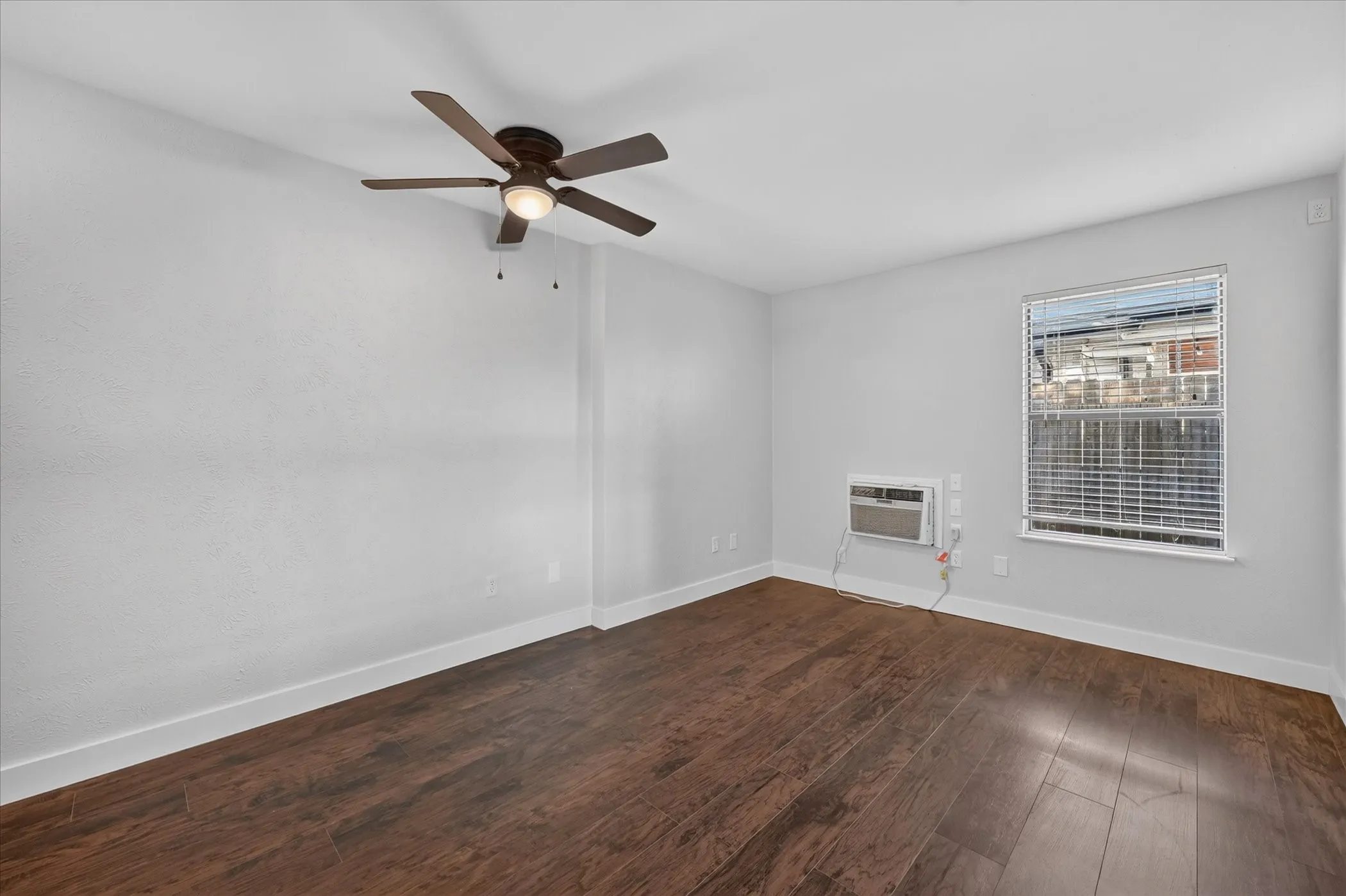 Wood-finish flooring, ceiling fan with integrated lighting, window with blinds, and window-mounted air conditioning unit