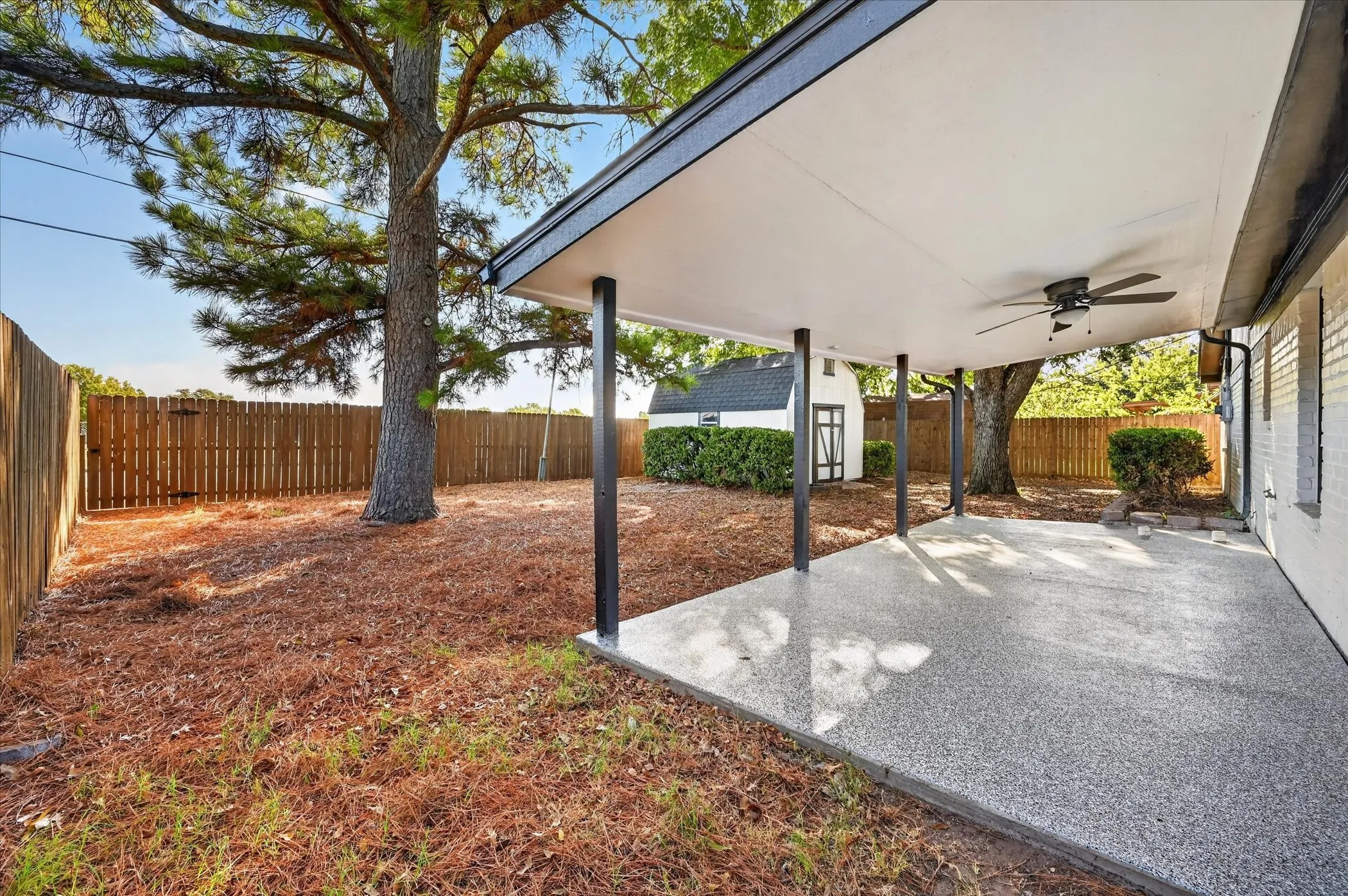 Covered patio with a ceiling fan, a private fenced yard, mature trees, and a detached storage shed