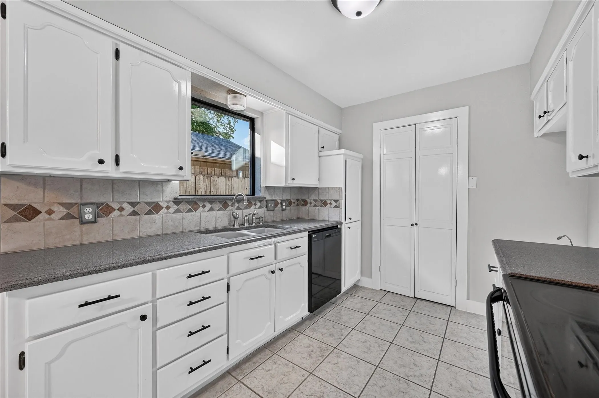 Kitchen featuring white cabinetry, dark countertops, tiled backsplash, and tile flooring