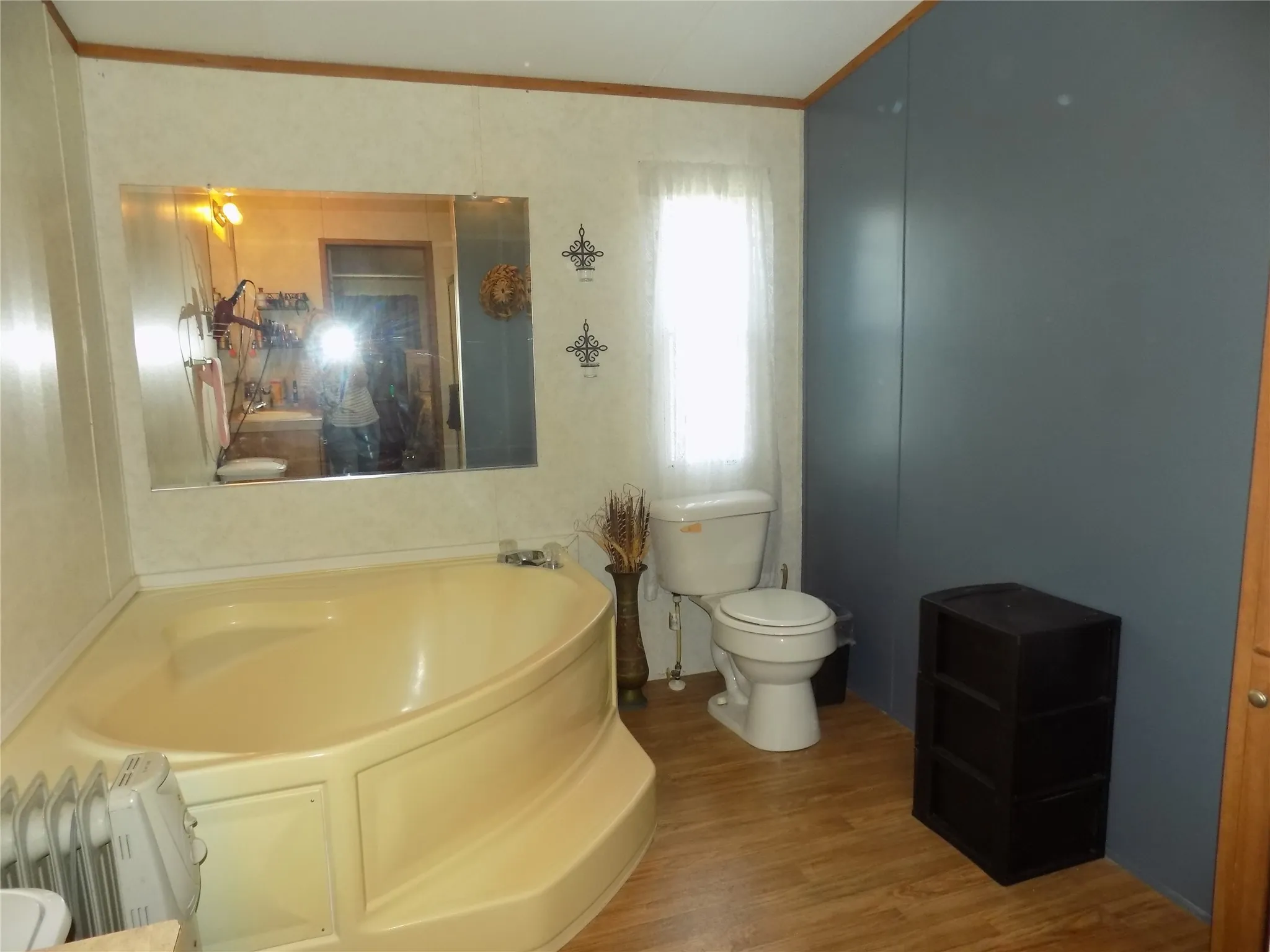 Corner garden tub with integrated steps, large wall-mounted mirror, and wood-finish flooring.