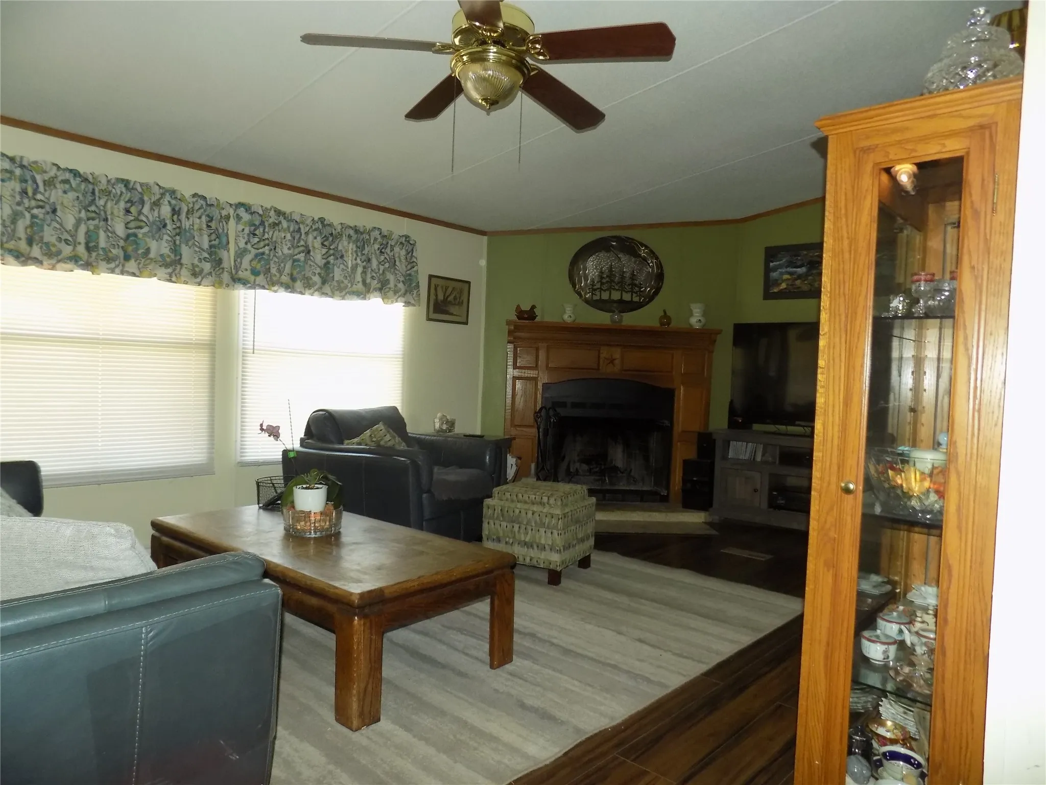 Wood-finish flooring, ceiling fan with light, and corner wood-framed fireplace with mantel.
