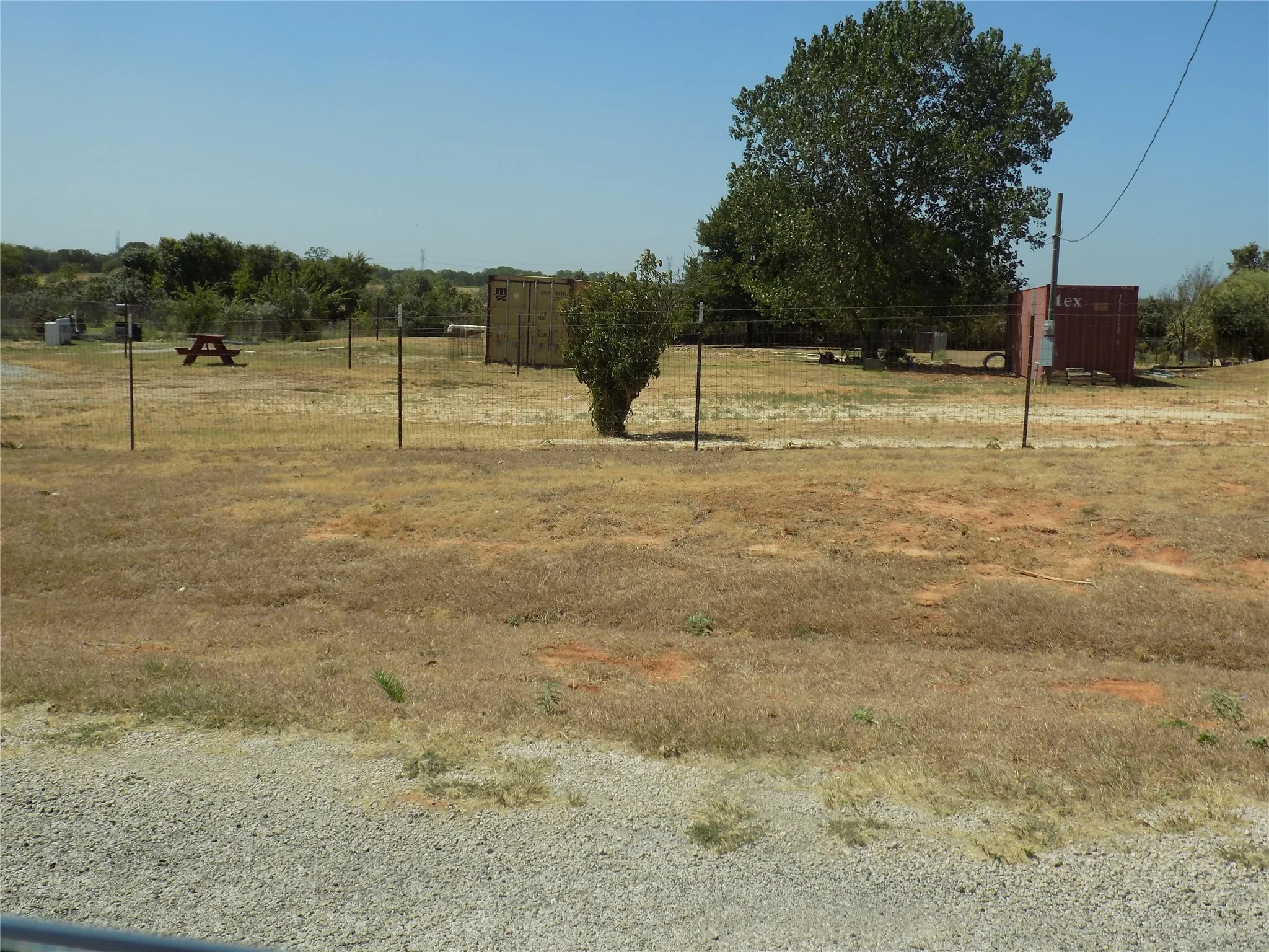 Expansive outdoor area featuring a large  tree, total exterior fencing, and a gravel entry.