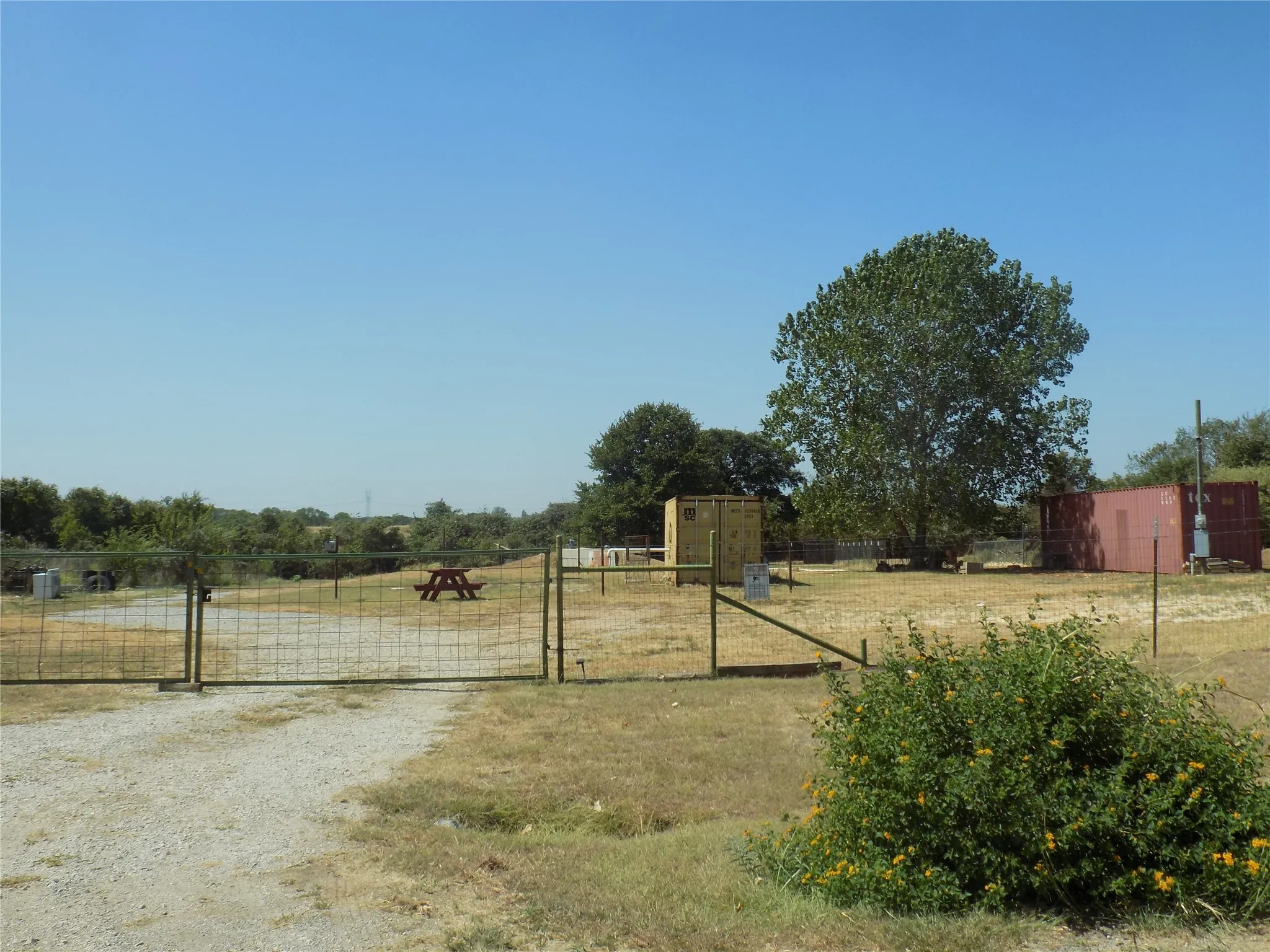 Gravel driveway with a metal gate and fencing, complemented by mature trees and natural vegetation.
