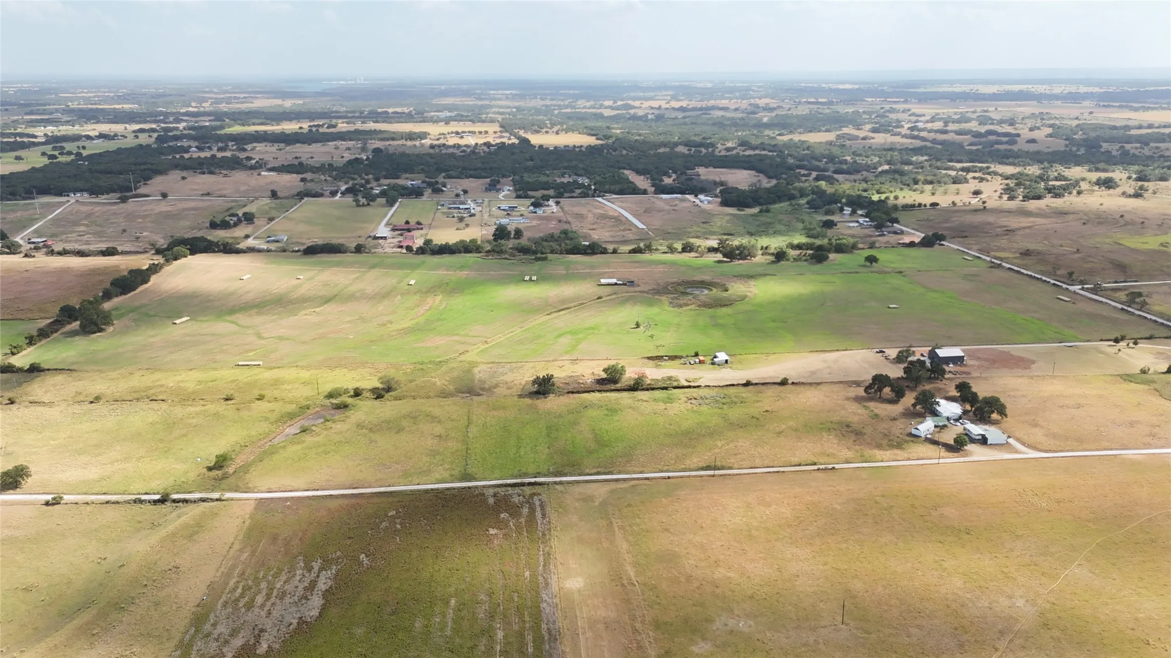 Expansive rural landscape featuring open fields, scattered trees, and distant structures