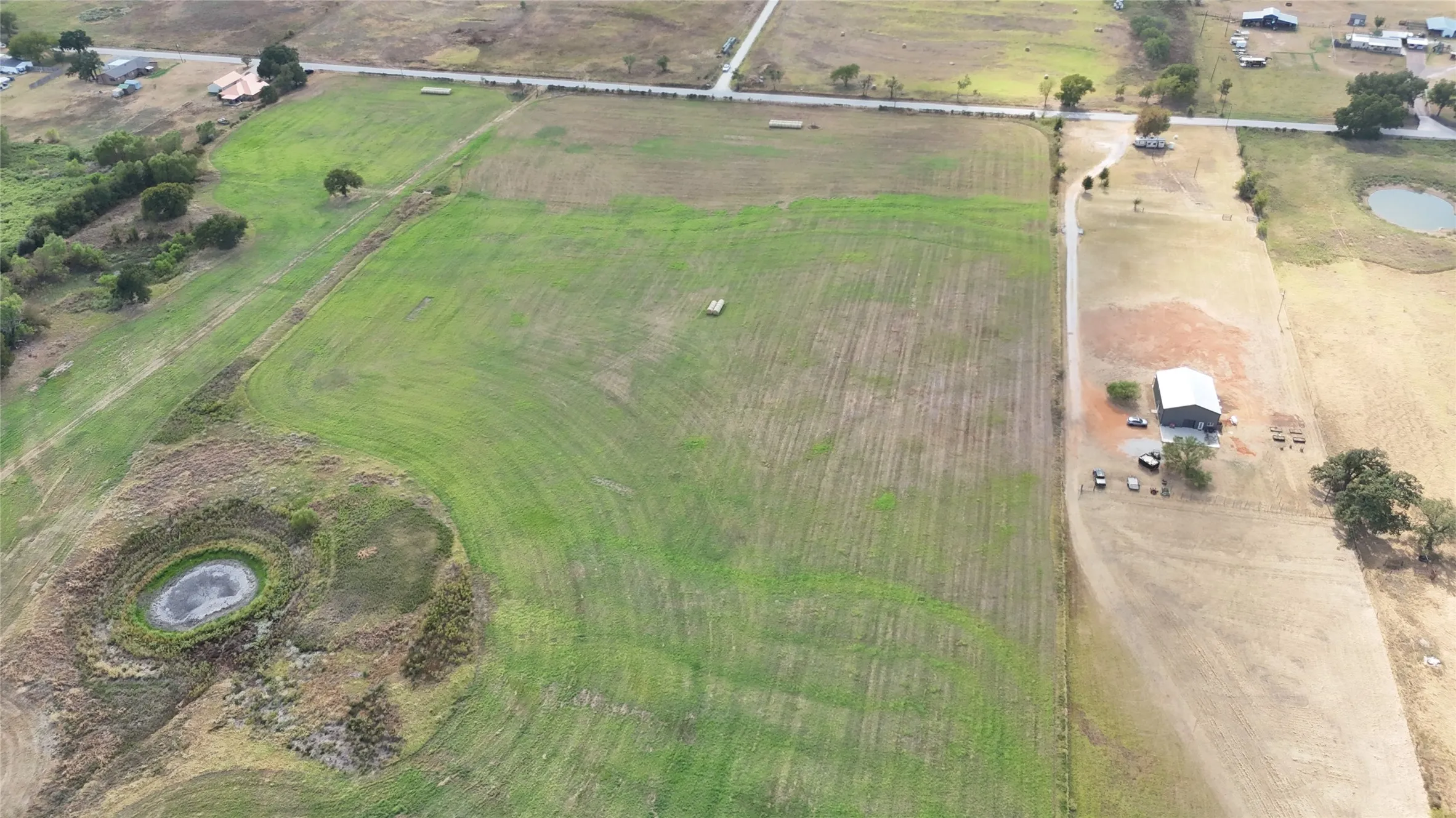 Expansive green fields, a small pond, an agricultural building, and a paved road