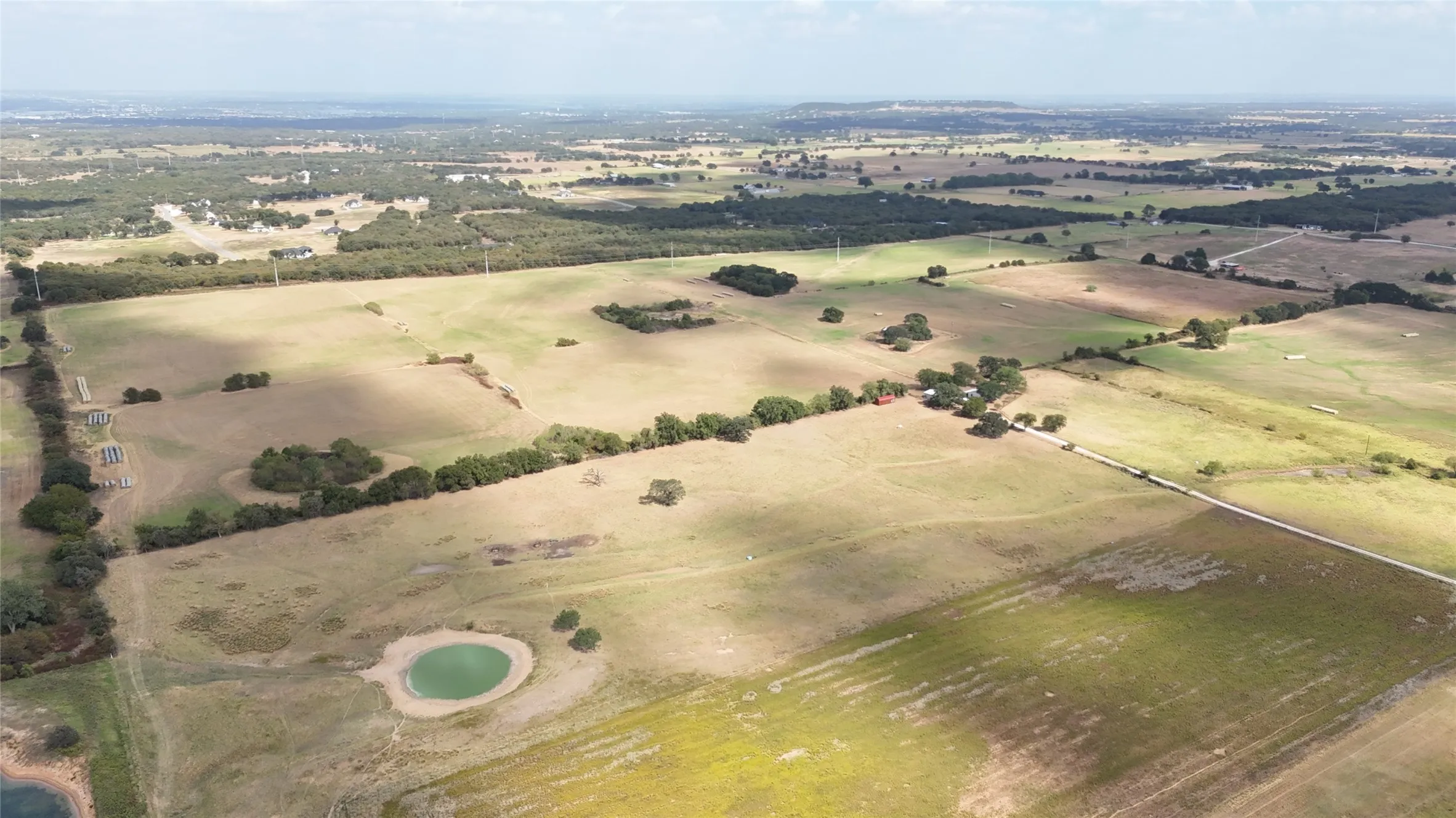 Expansive rural landscape featuring a natural pond, scattered mature trees, and varying terrain