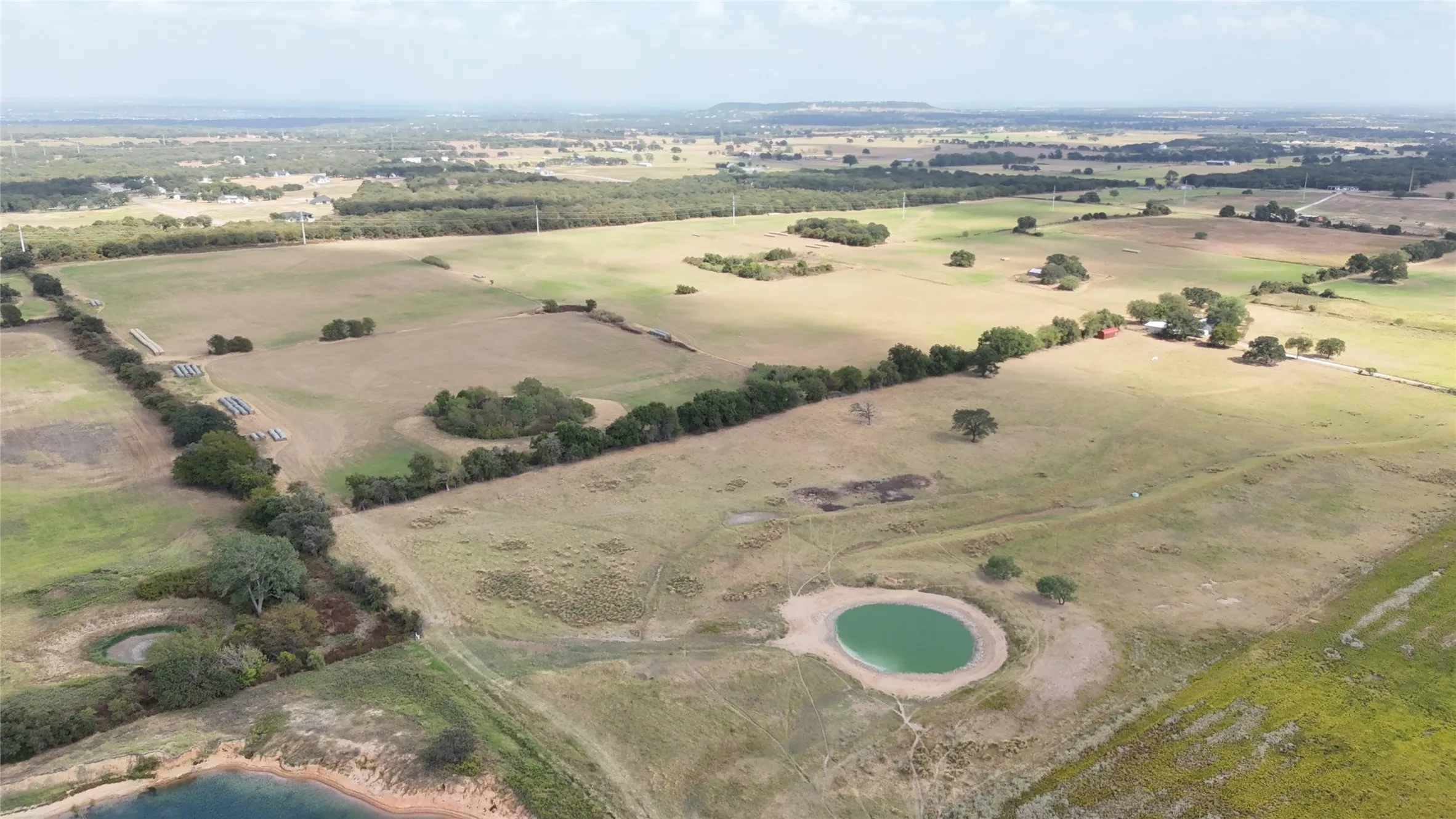 Expansive rural landscape featuring a pond, scattered mature trees, and a distant residence