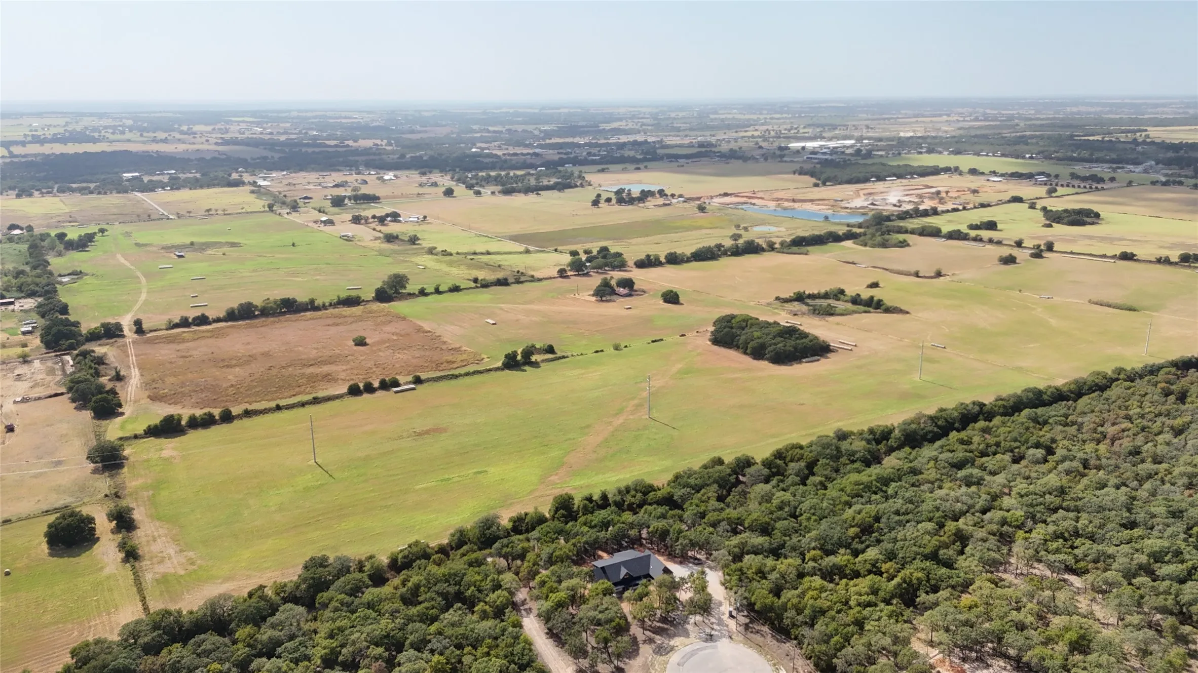 Expansive rural landscape featuring open fields, scattered mature trees, and natural wooded areas