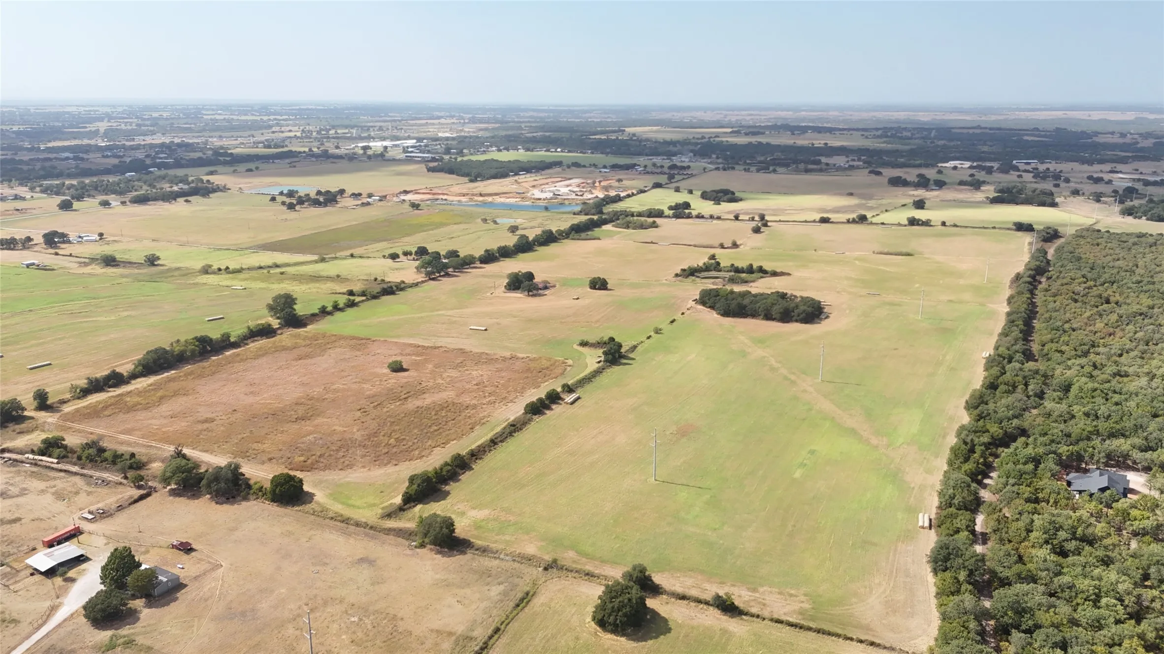 Expansive acreage featuring open fields, clusters of mature trees, and a residential structure nestled within a densely wooded area