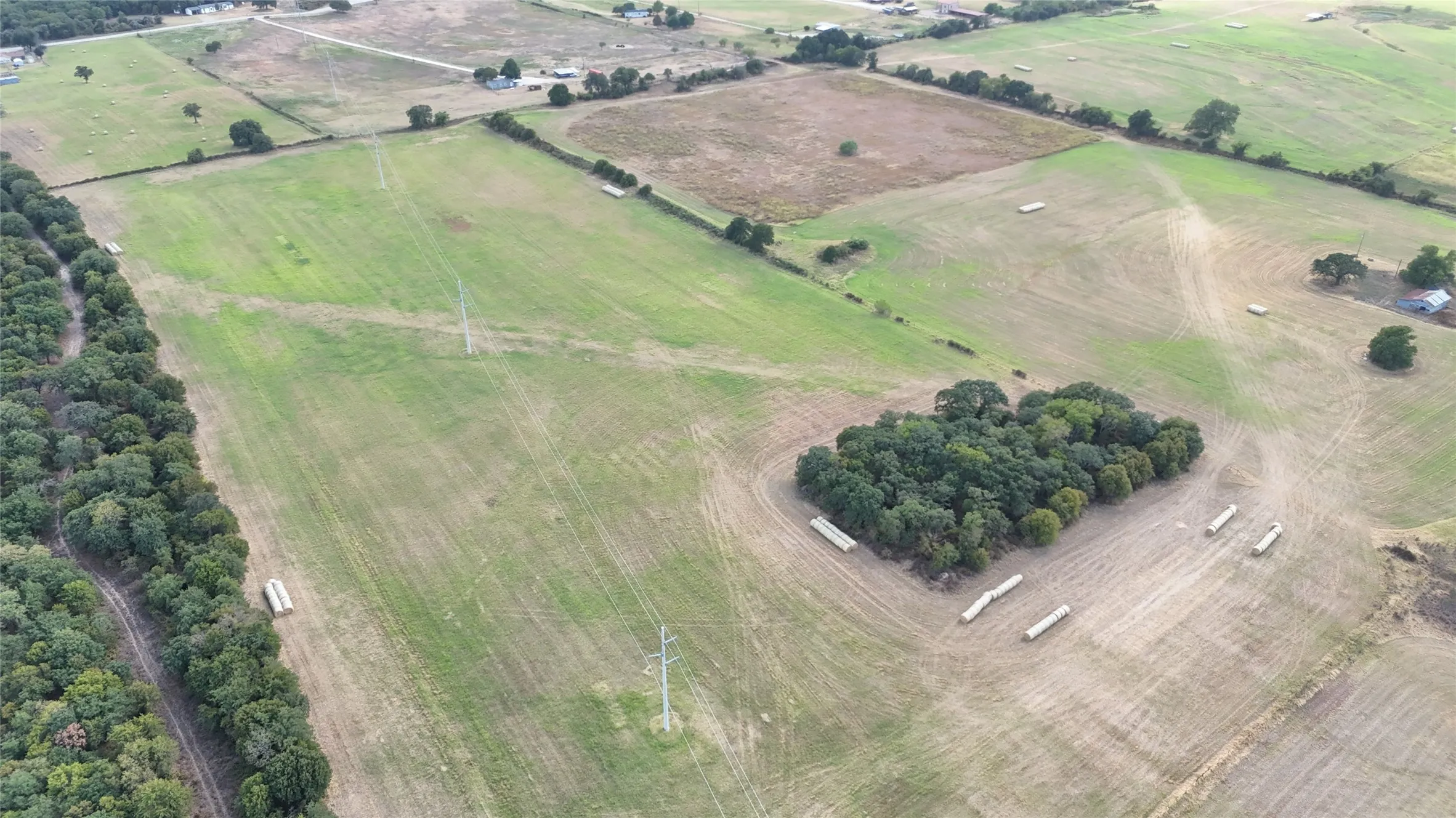 Expansive rural acreage featuring cultivated fields, mature tree lines, and a central wooded cluster