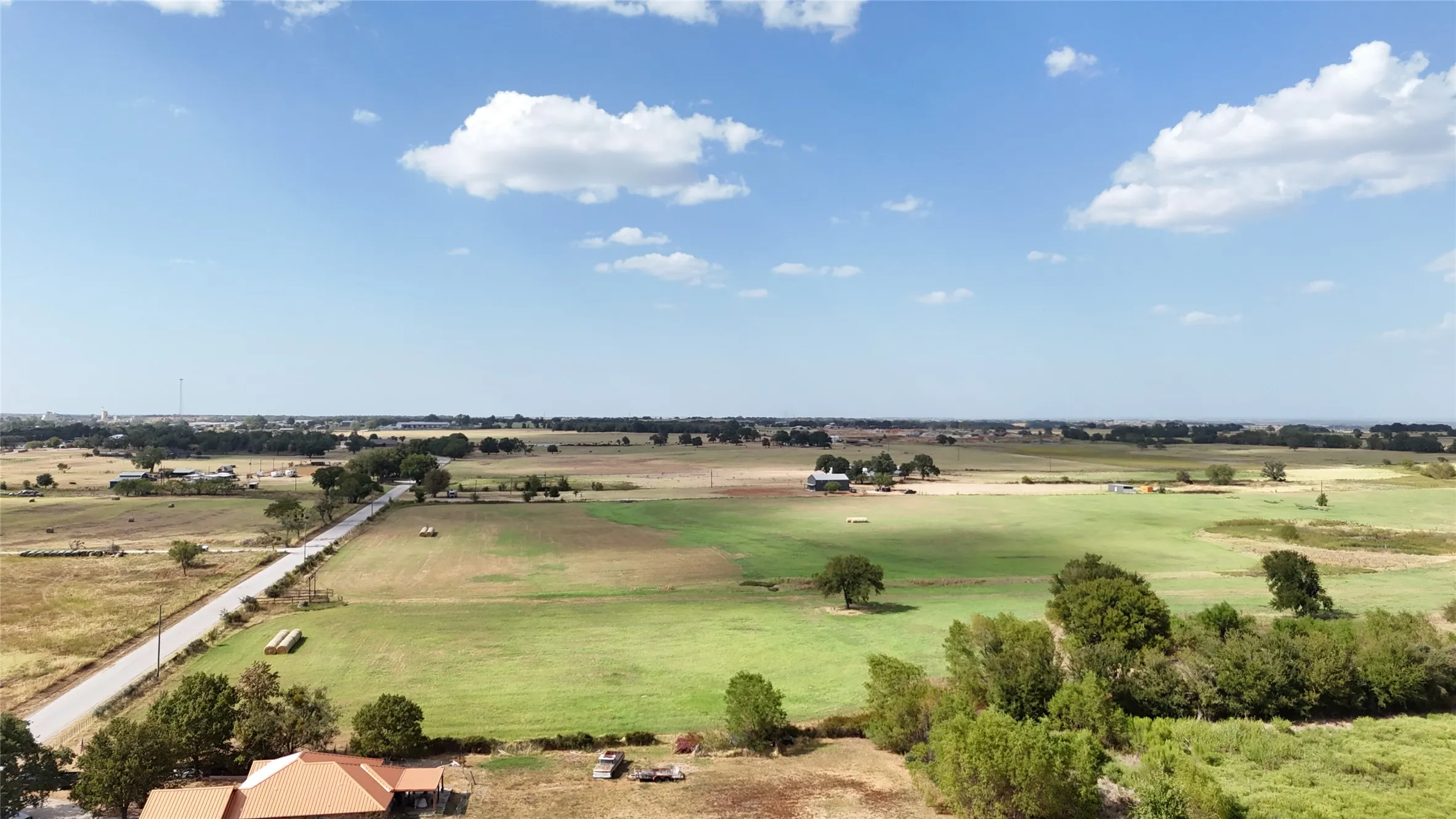 Expansive acreage featuring a paved road, mature trees, and agricultural fields