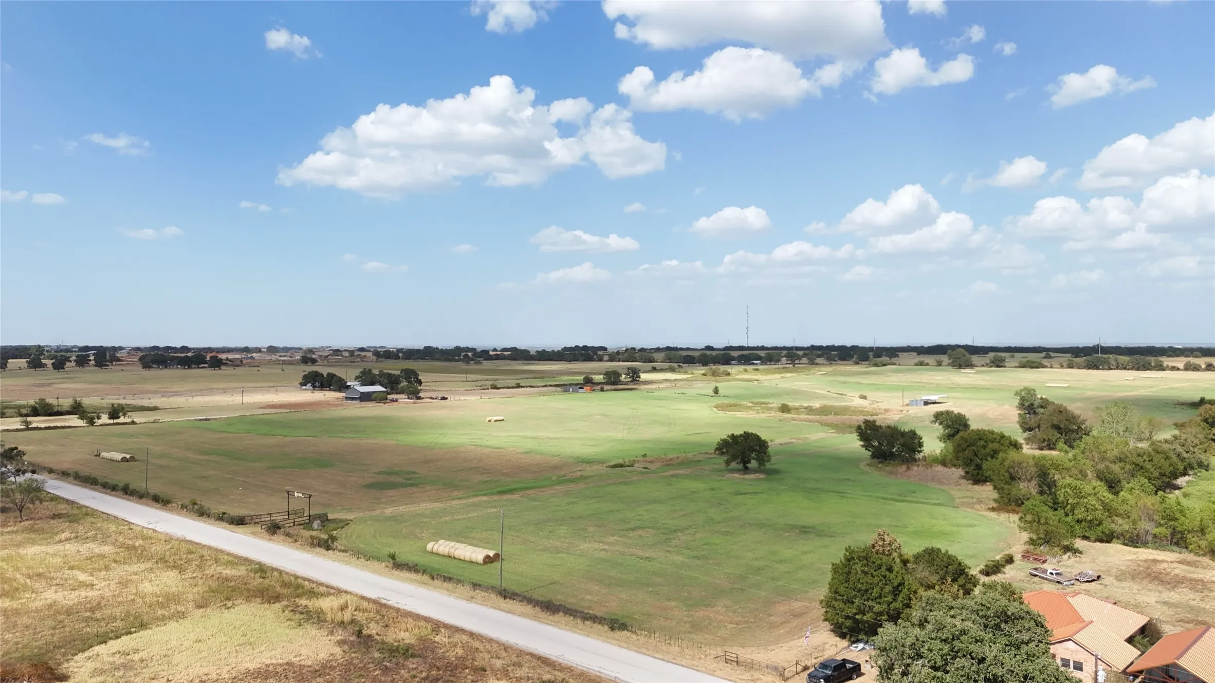 Expansive rural acreage featuring green pastures, scattered mature trees, and a paved road