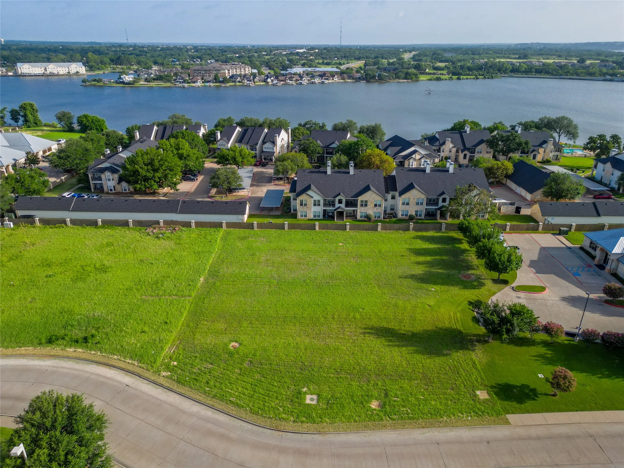 Expansive green lot with established perimeter fencing, bordered by a paved roadway and mature trees