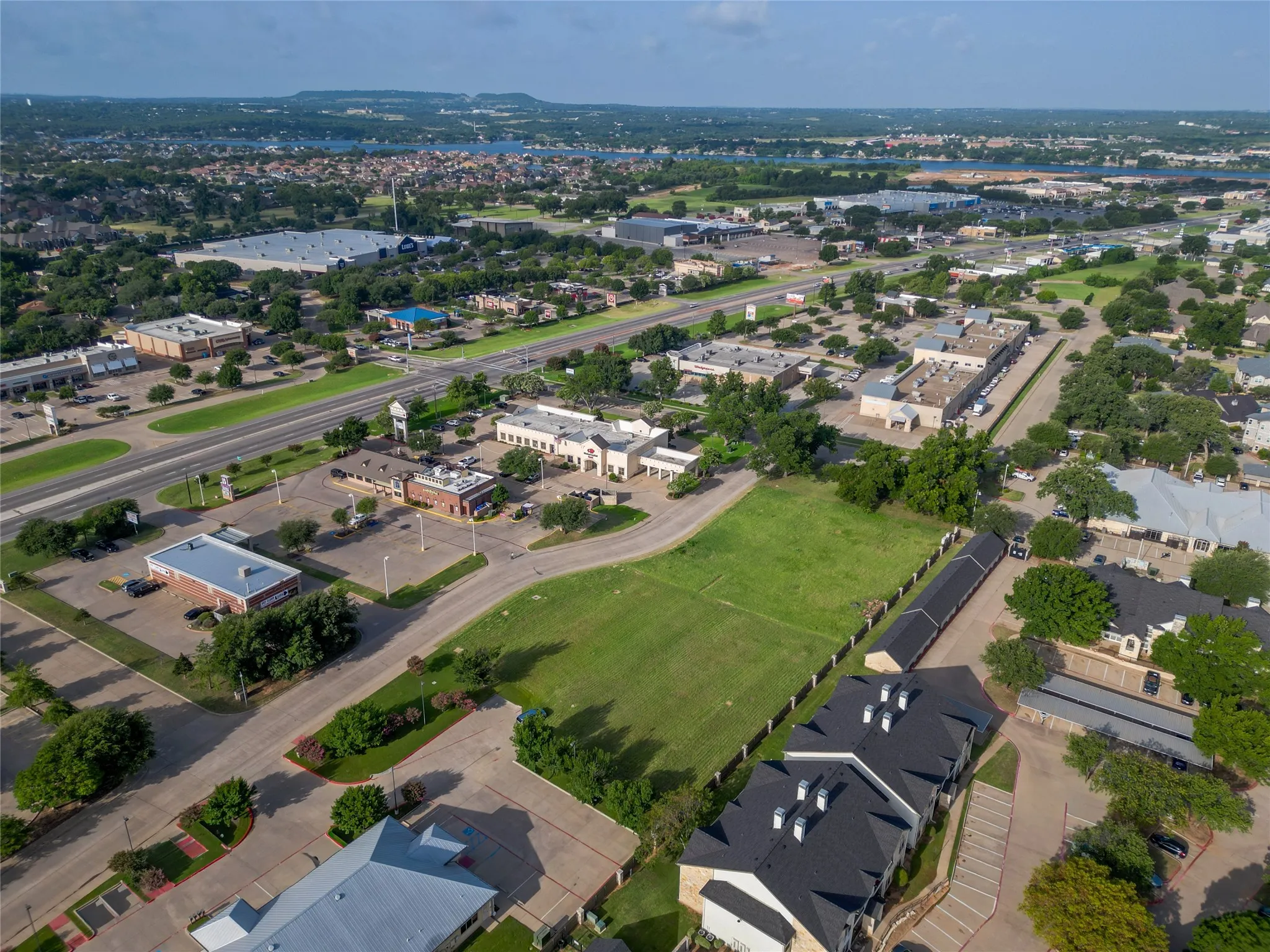 Expansive open lot with a green lawn, bordered by a dark fence, and surrounded by commercial properties