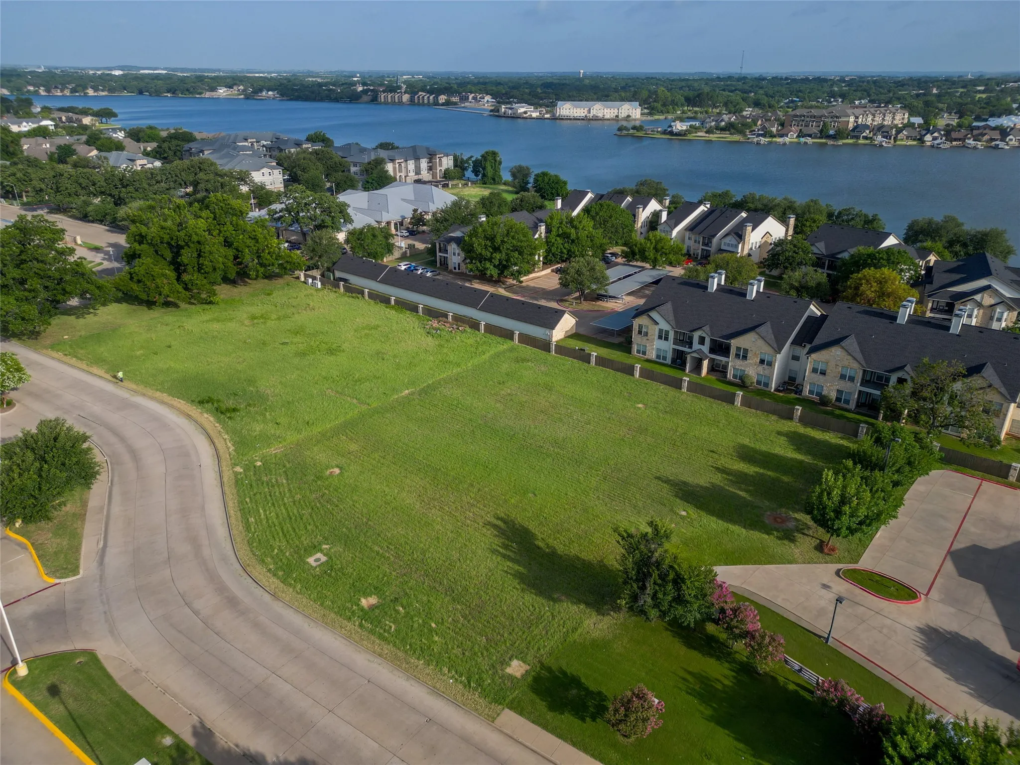 Expansive green space featuring a large grassy lot, paved road frontage, and a backdrop of​​‌​​​​‌​​‌‌​‌‌​​​‌‌​‌​‌​‌​​​‌​​ water