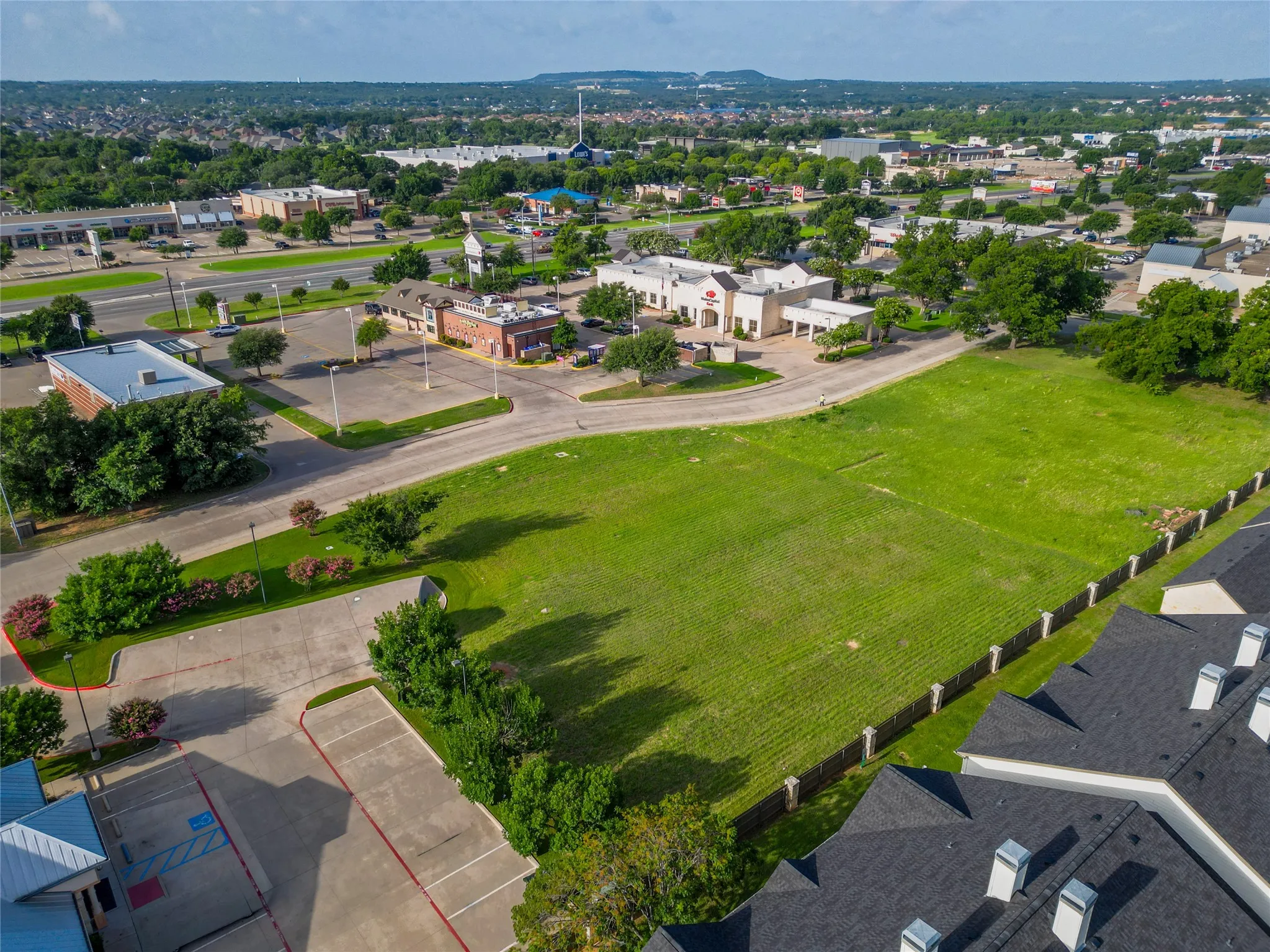Expansive green space with perimeter fencing, surrounded by paved roadways and adjacent commercial structures