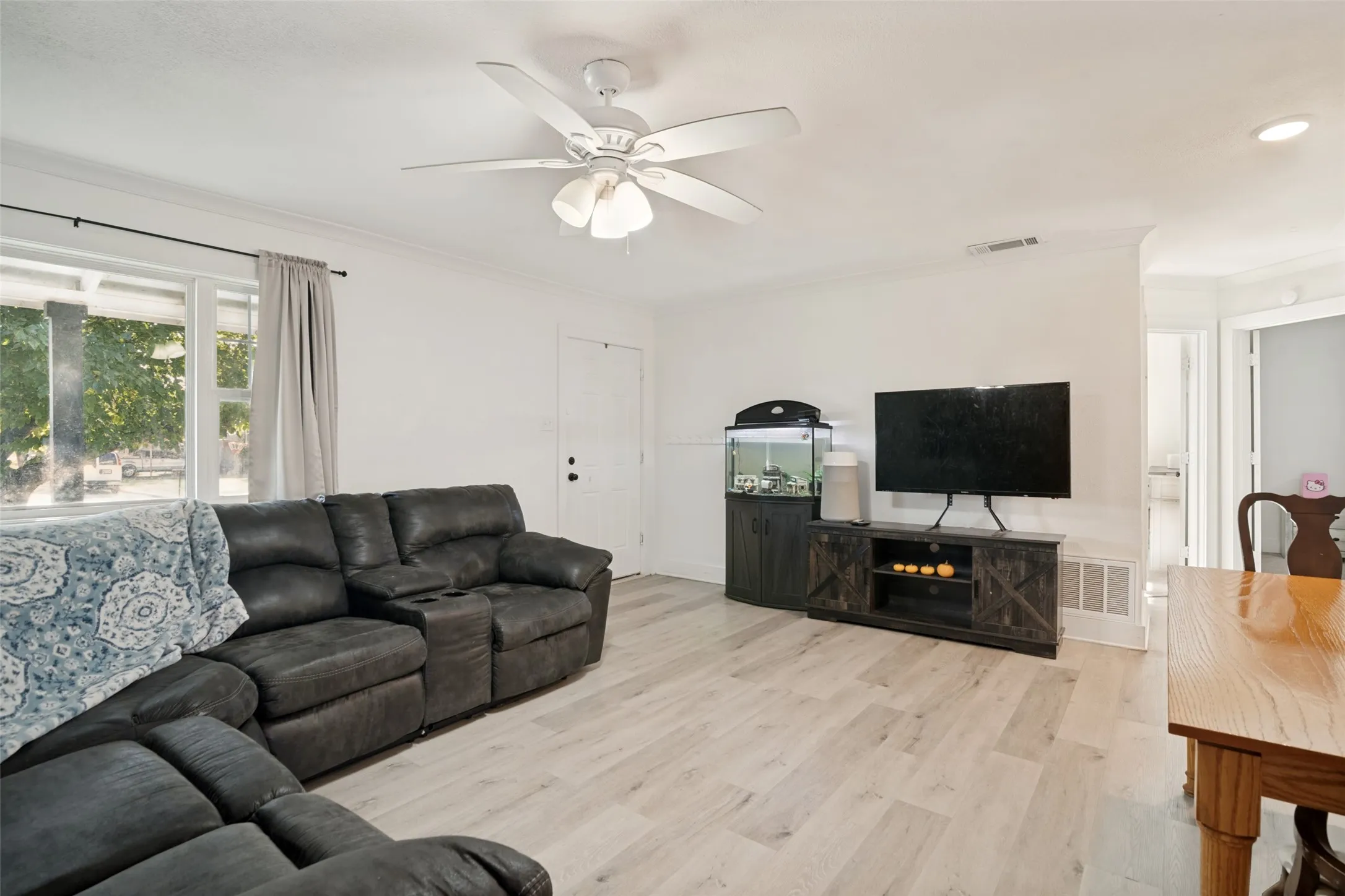 Spacious living room featuring large picture window, LVP flooring, and ceiling fan.