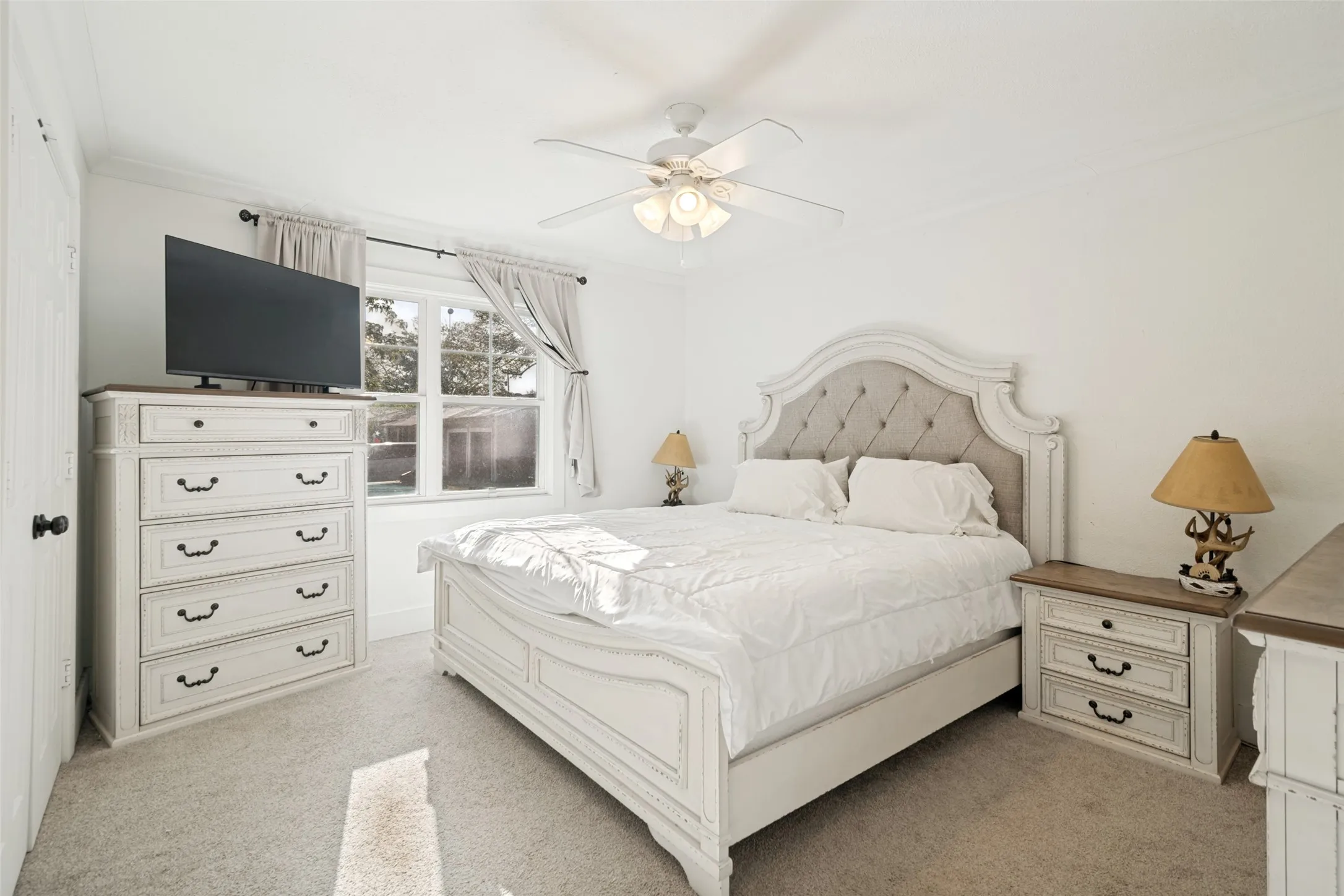 Primary bedroom with carpet flooring, crown molding, and a ceiling fan with integrated lighting.