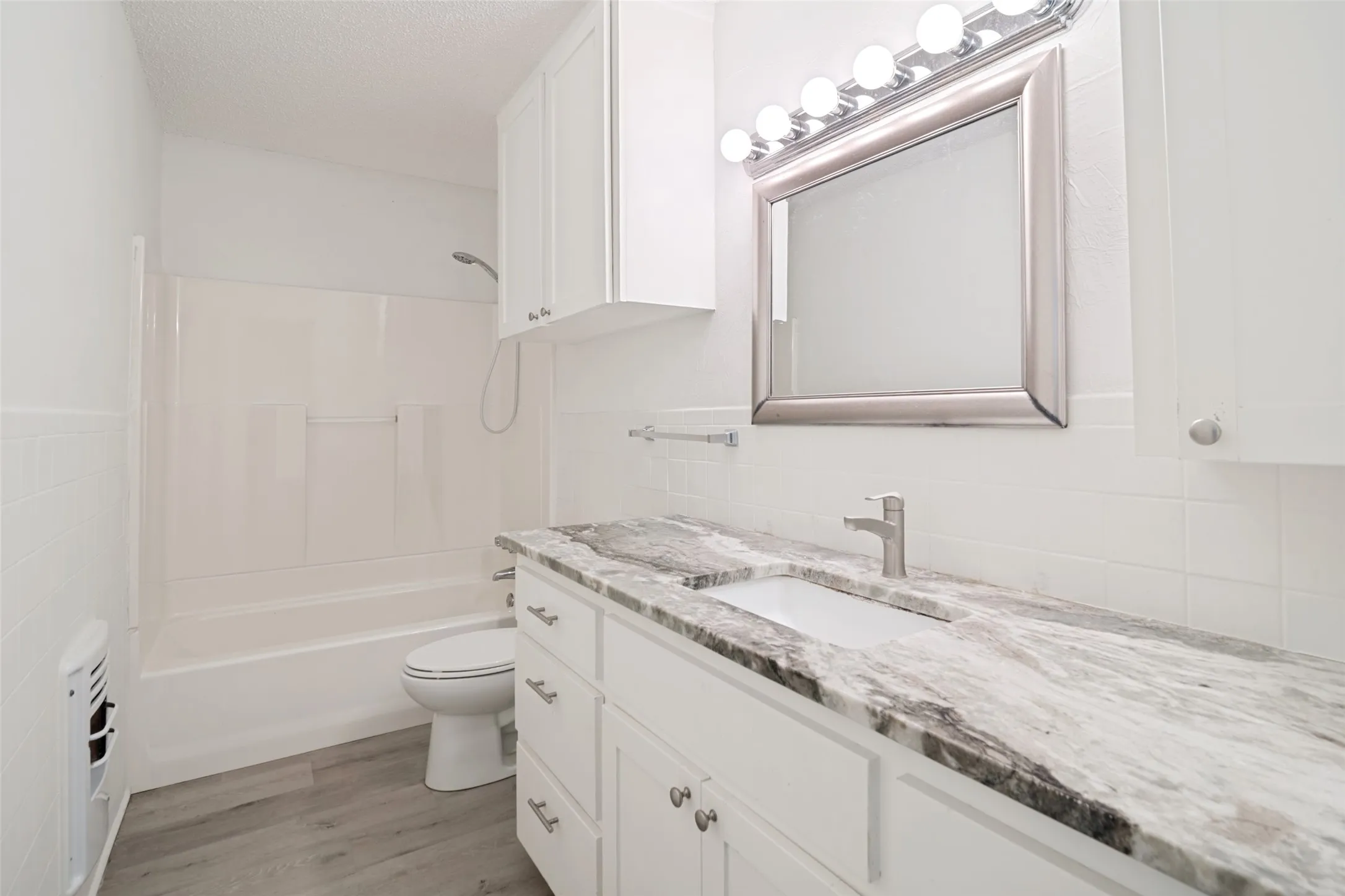 Practical and functional bathroom with white shaker-style vanity with brushed nickel hardware, integrated rectangular sink, gray-patterned countertop, and wood-finish flooring.