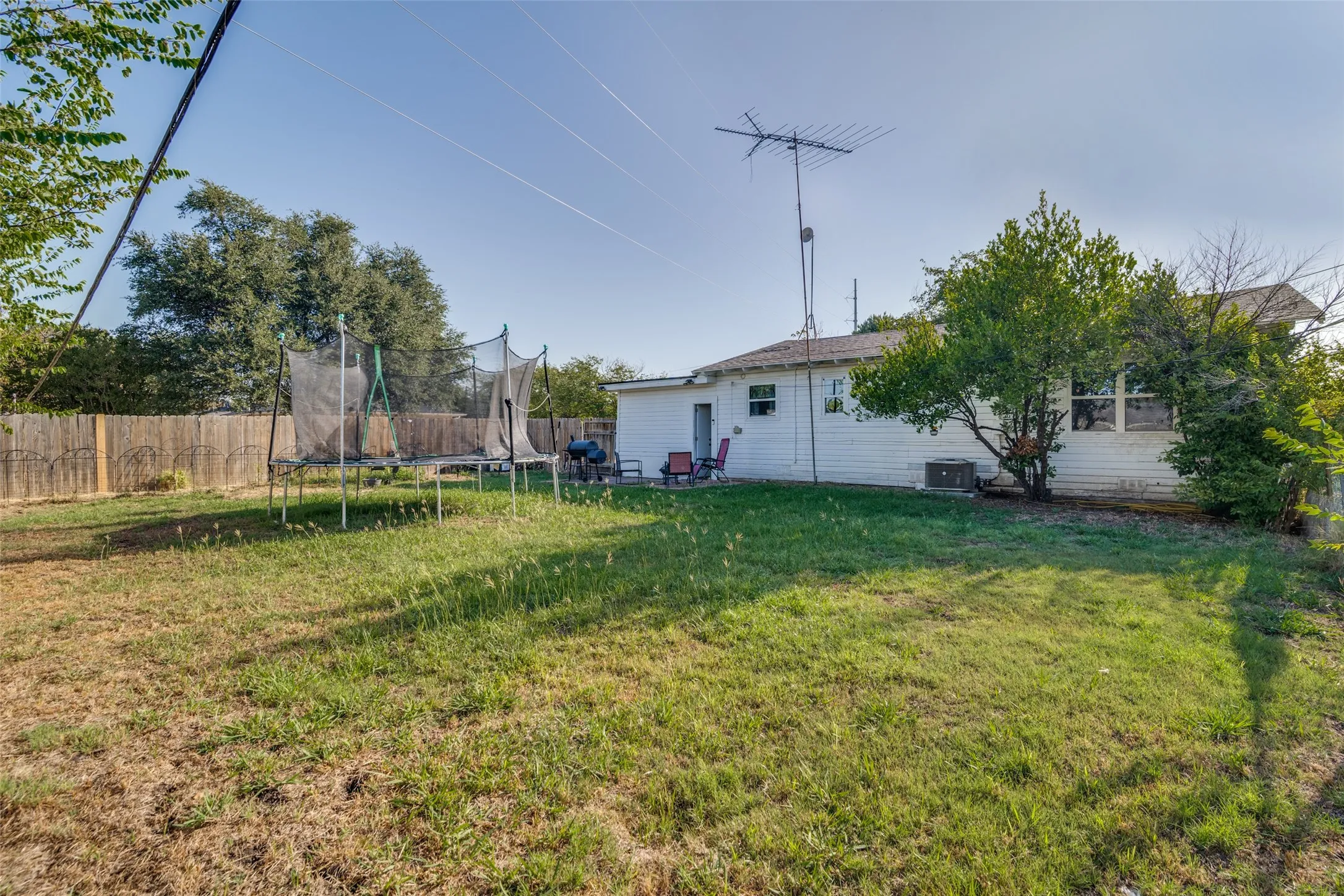 Expansive grassy yard with mature trees and a wood fence.