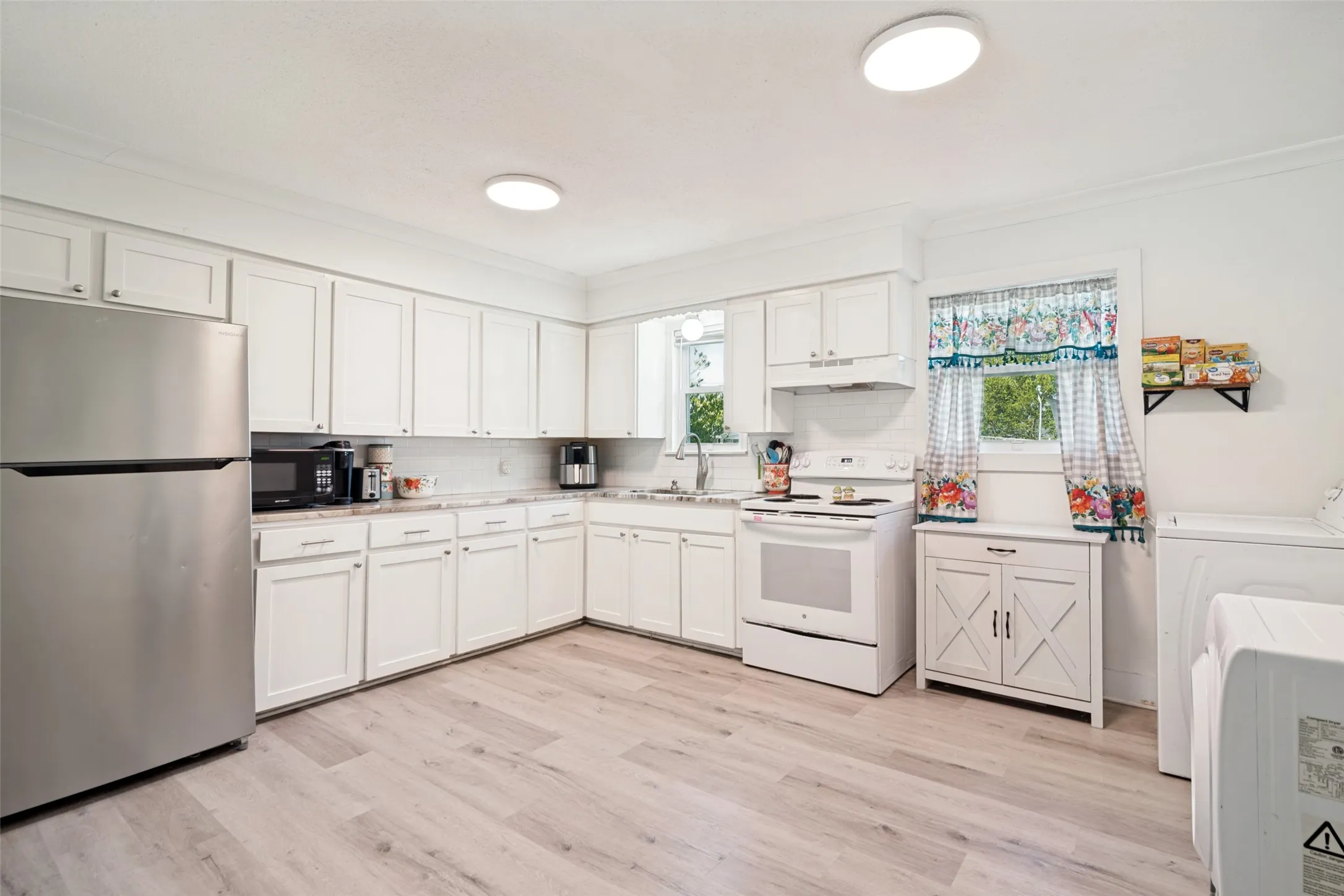 Kitchen featuring white cabinetry, light-toned wood-finish flooring, white range, and white subway tile backsplash.