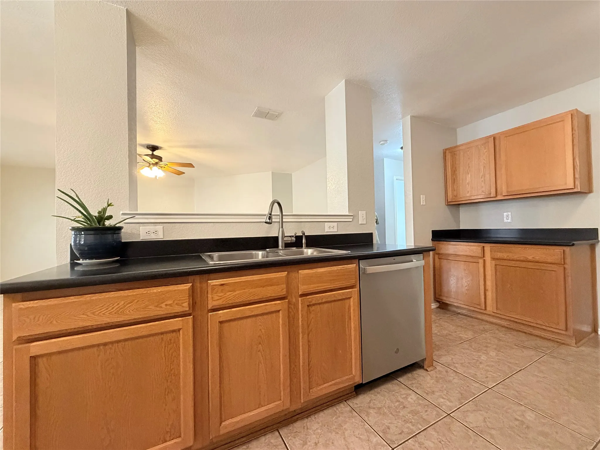 Kitchen featuring wood-finish cabinetry, dark countertops, a stainless steel sink with a high-arc faucet, and tiled flooring