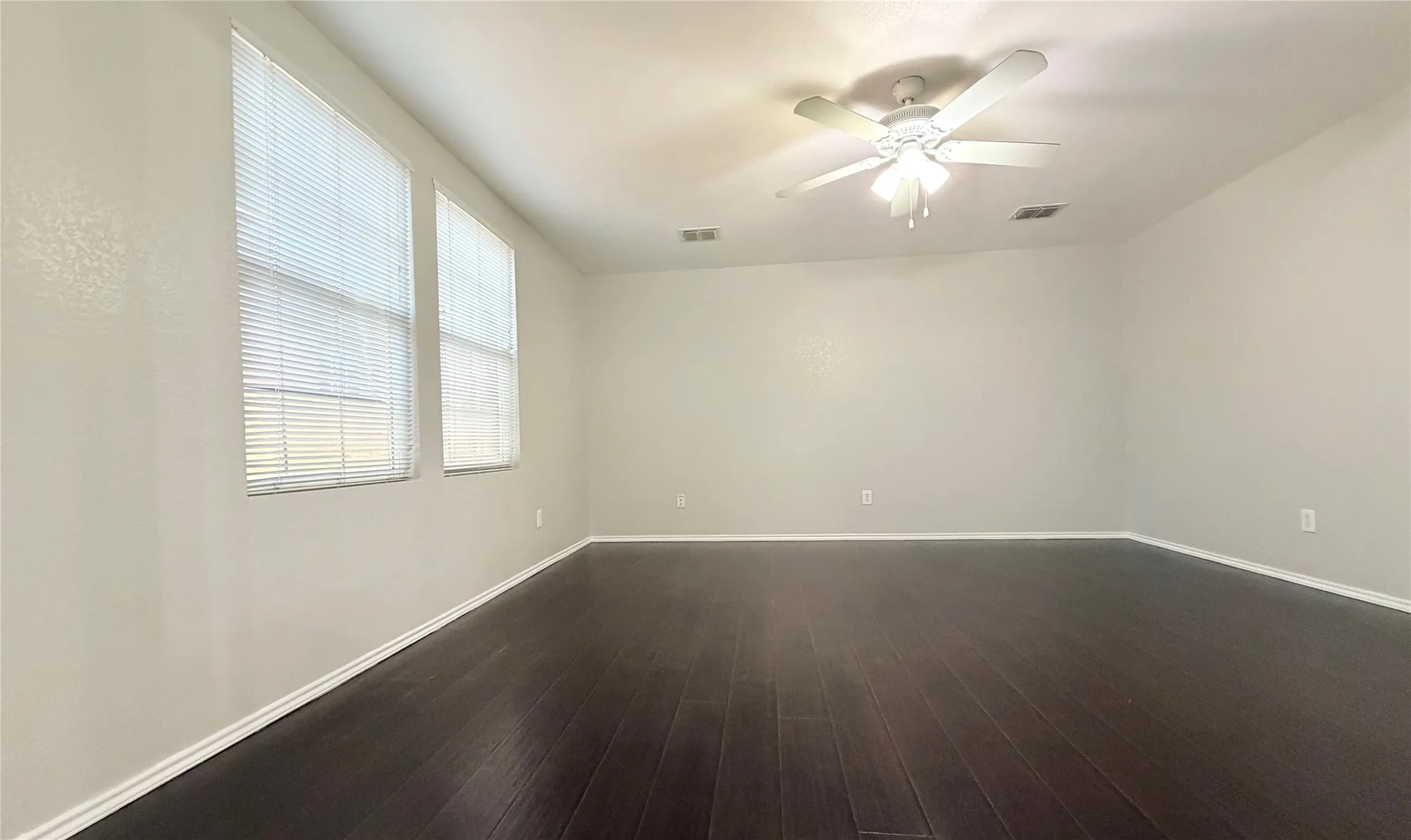 Spacious  master room featuring wood-finish flooring, light-toned walls, multiple windows with blinds, and a ceiling fan with integrated lighting