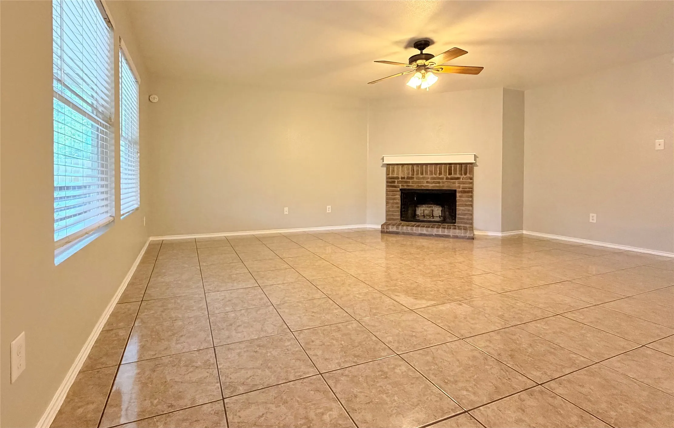 Spacious room featuring tile flooring, a brick fireplace with a white mantel, and multiple windows
