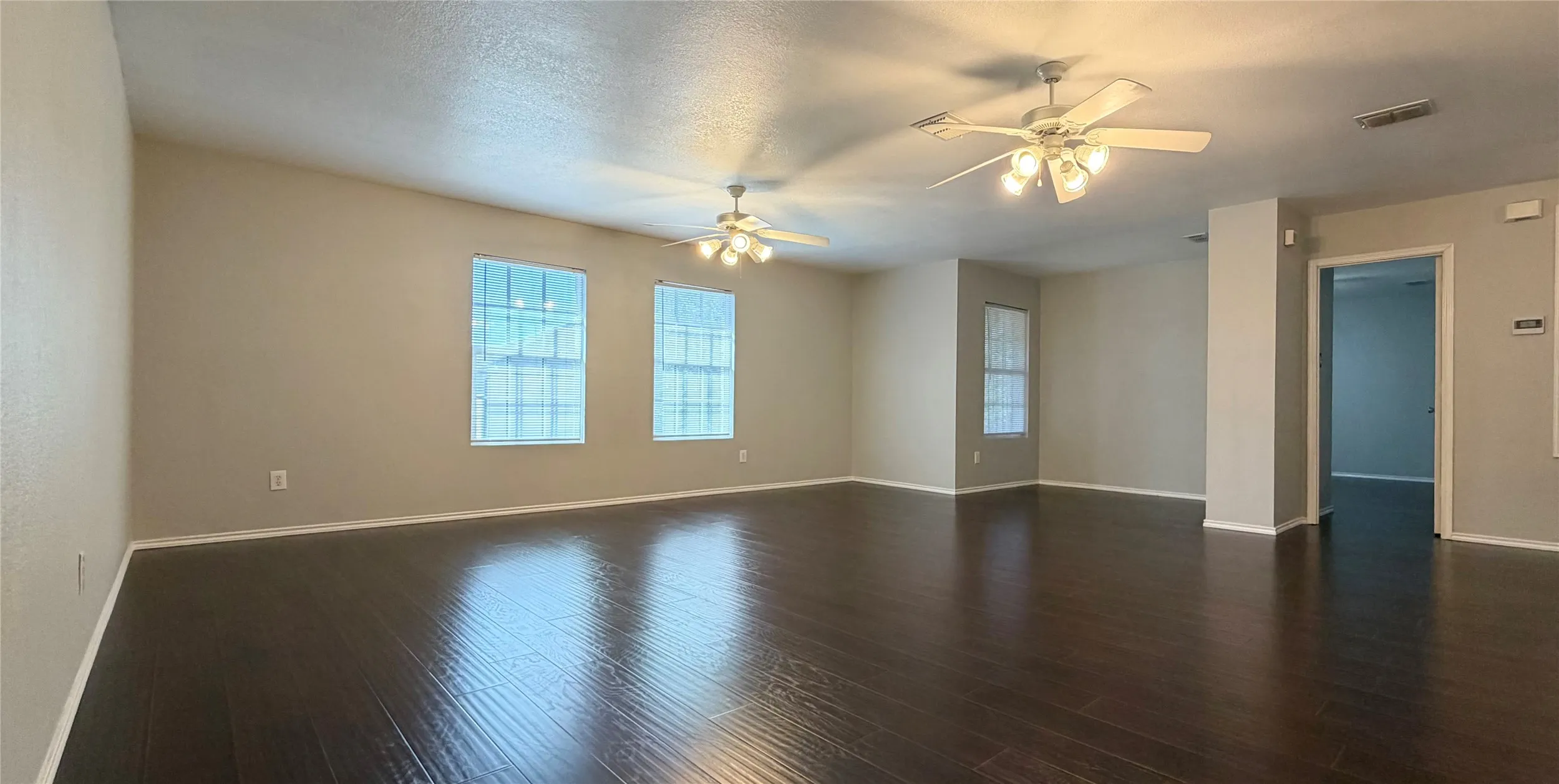Upstarirs spacious game room/living area featuring wood-finish flooring, multiple windows, and two ceiling fans with integrated lighting